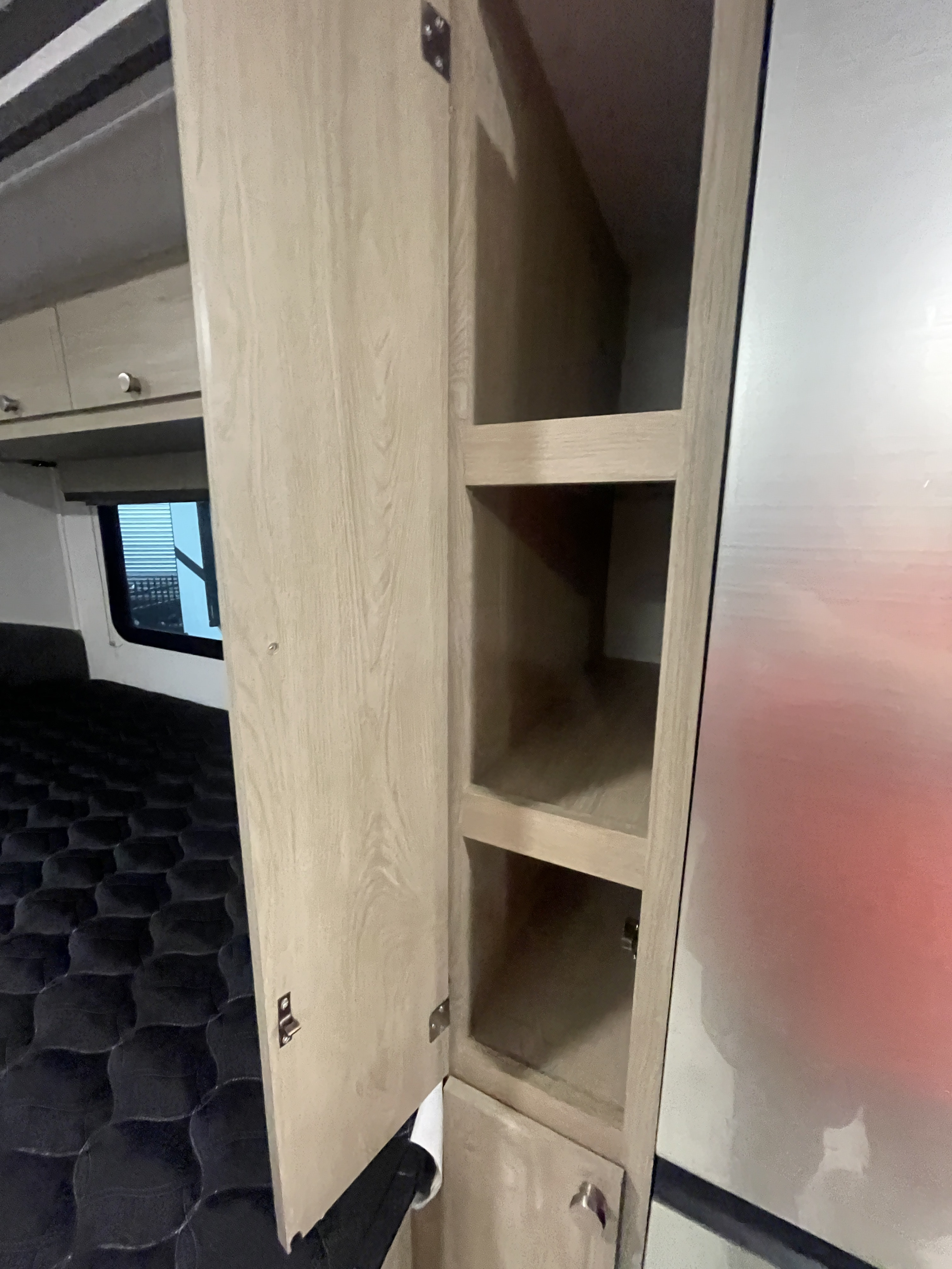 RV rental: Open light wood cabinet with shelving next to a quilted bed, offering compact storage.. Coachmen LEPRECHAUN 230FS 2026
