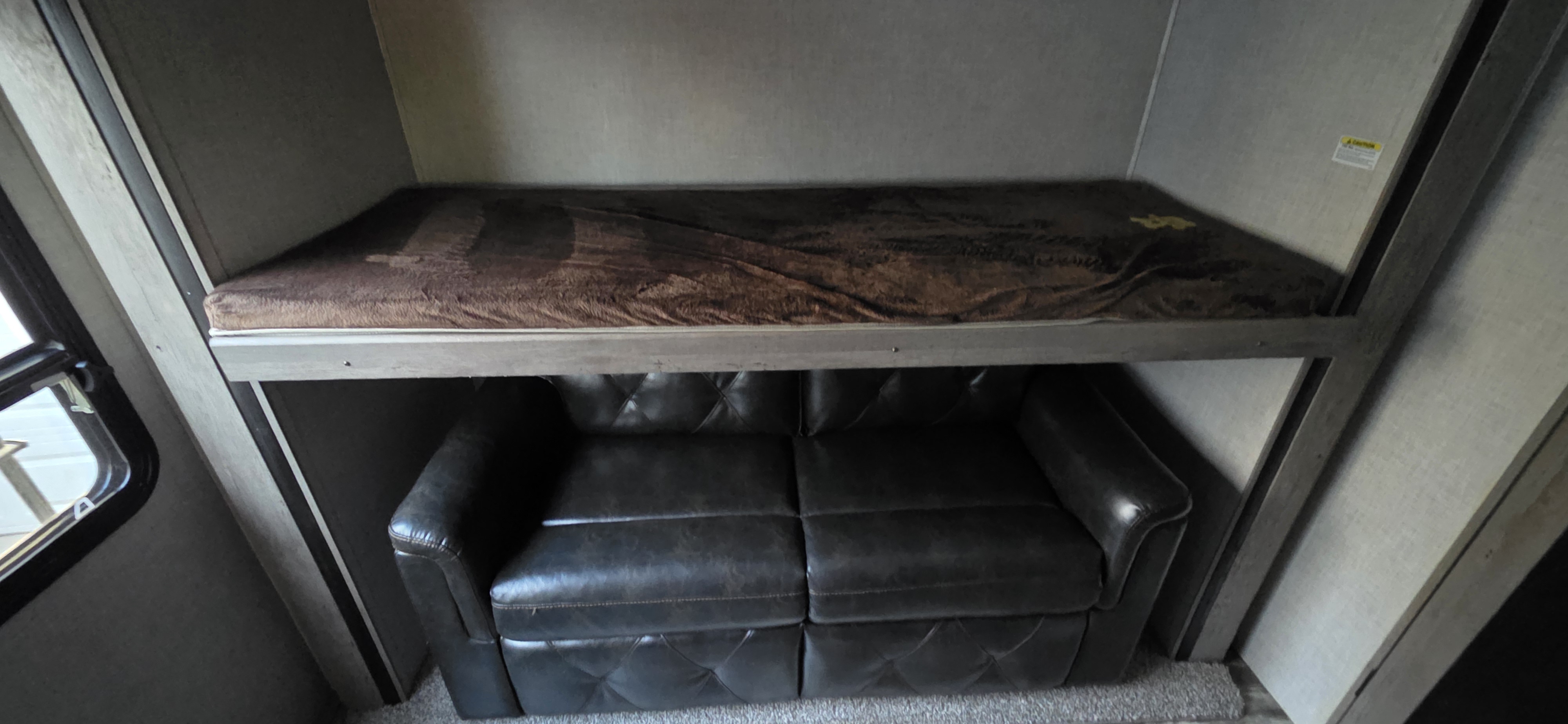 RV rental bunk bed with brown bedding sits above a dark leather sofa, showcasing compact interior design.. Keystone RV Keystone Outback 340bh 2020
