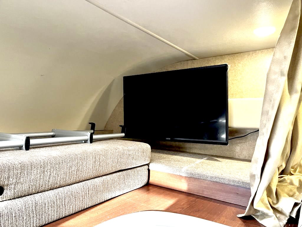 Cozy rv rental interior featuring a mounted TV, a folded bed with an aluminum ladder, and curtains in a sleeping nook.. Thor Freedom Elite 2017