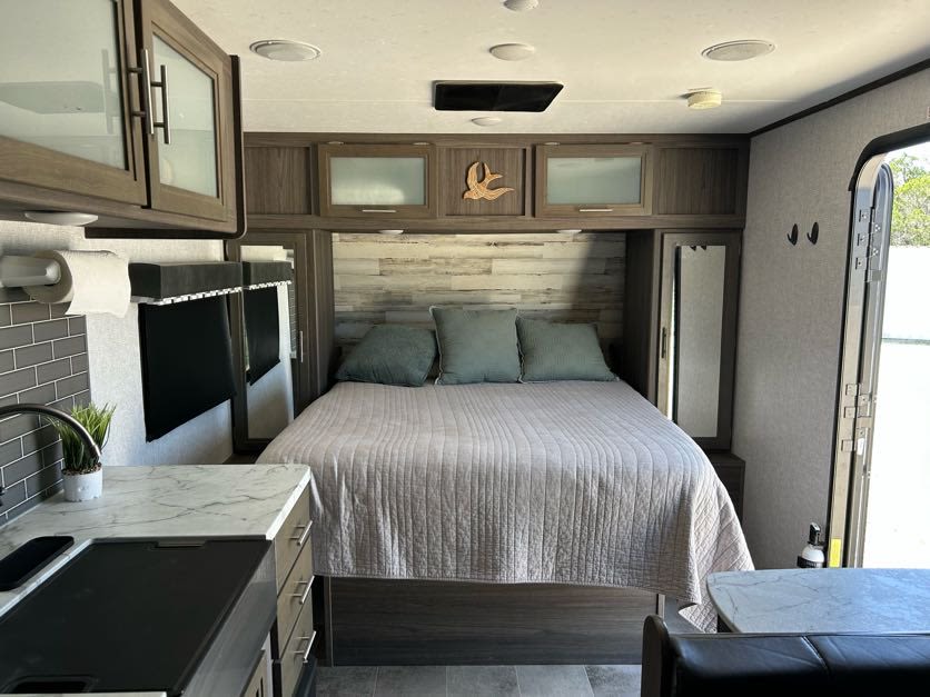 This RV rental interior features a bed with teal pillows, overhead cabinets, a gray tiled kitchen area, and dining space.. Dutchmen Kodiak ultralight 2021