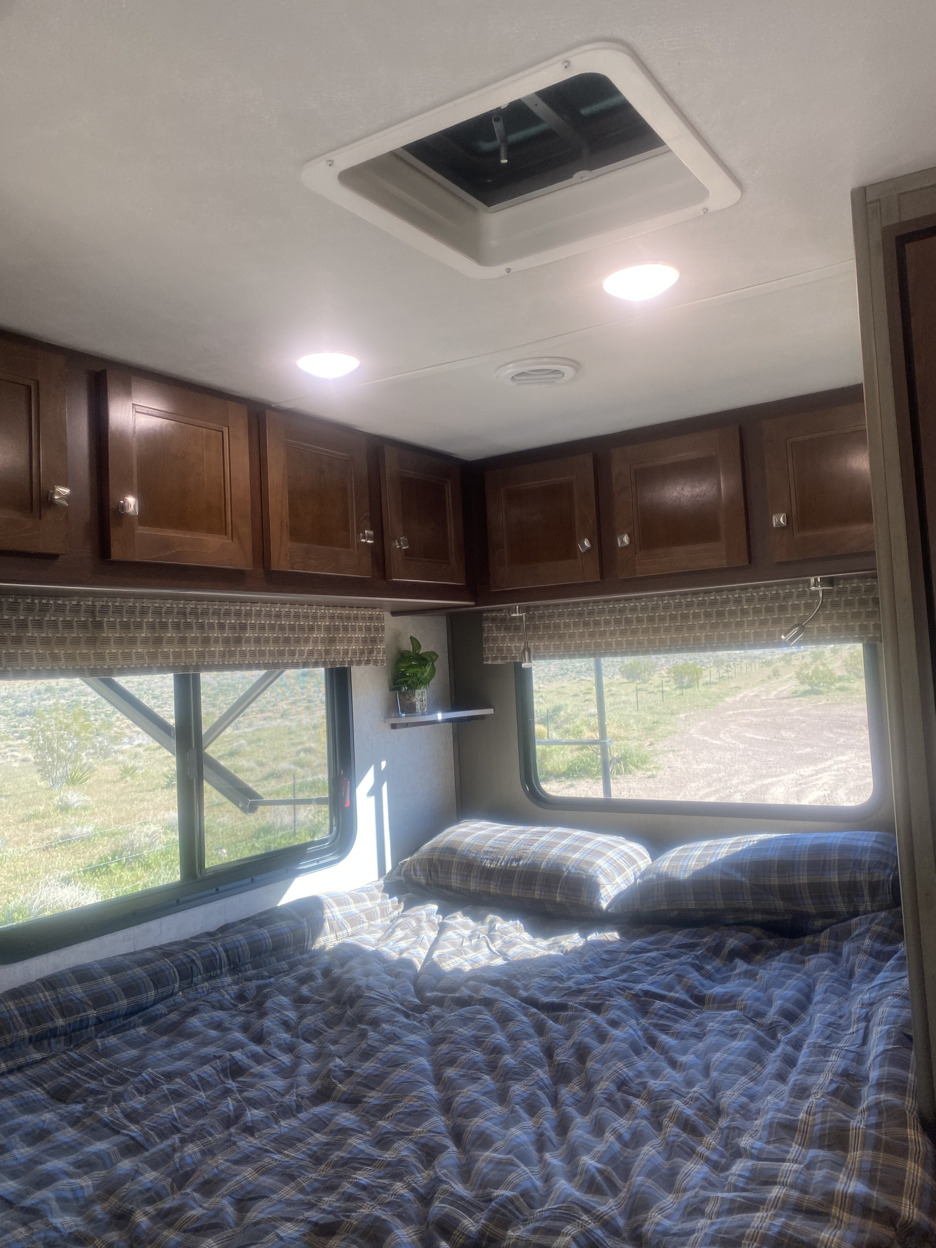 Relax in this comfortable RV rental bedroom, featuring plaid bedding, overhead storage, and large windows with a scenic view.. Forest River Sunseeker Classic 2020