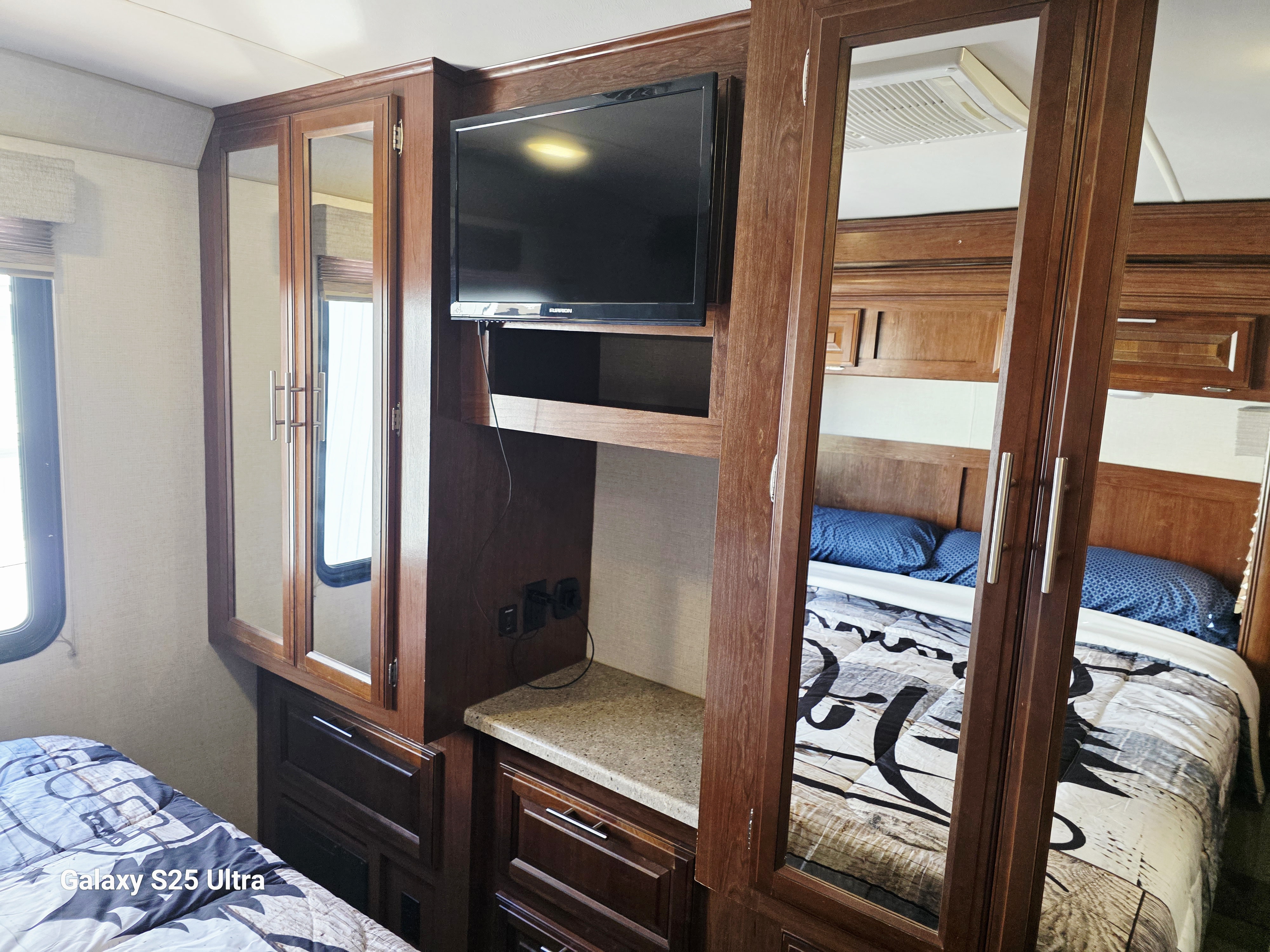 Inside an RV rental: a cozy bedroom with a TV, built-in storage, and a mirrored wardrobe reflecting the patterned bed.. Forest River FR3 30DS 2017