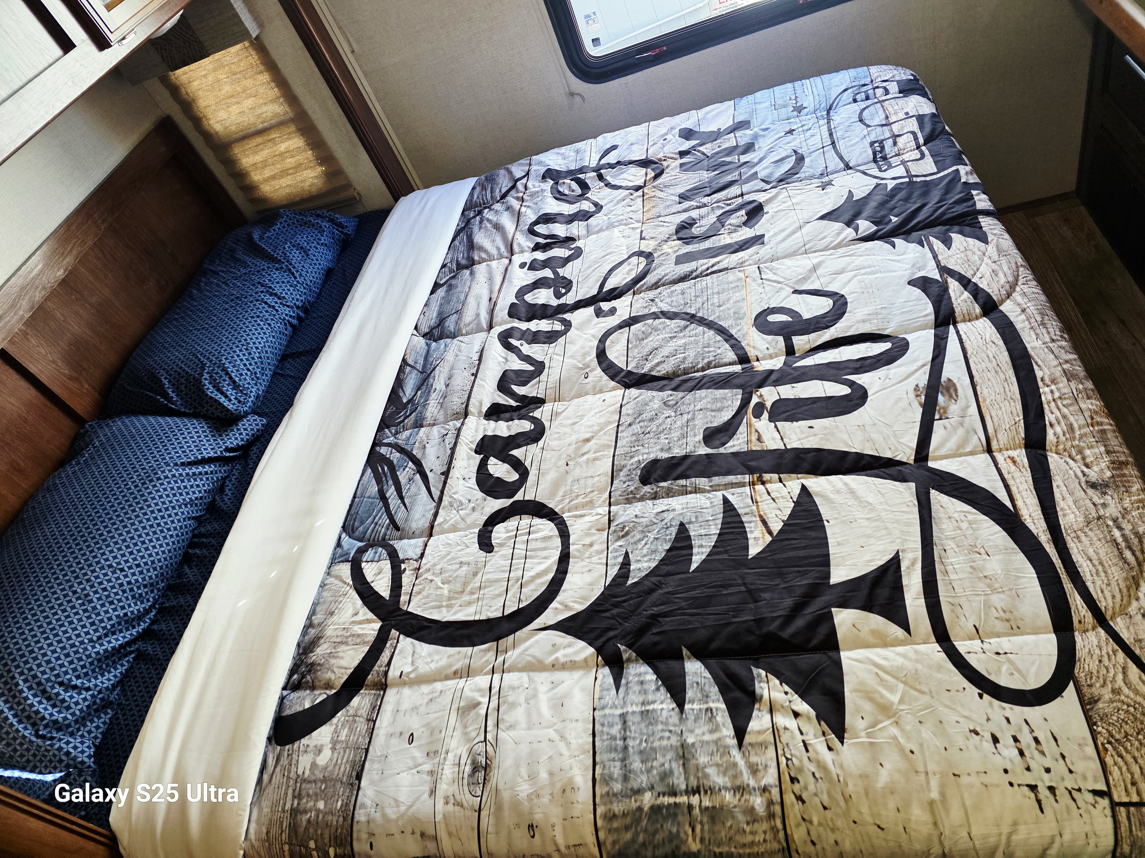 A cozy bed in an RV rental, featuring a "Camping Is Life" comforter and blue pillows, ready for your next adventure.. Forest River FR3 30DS 2017