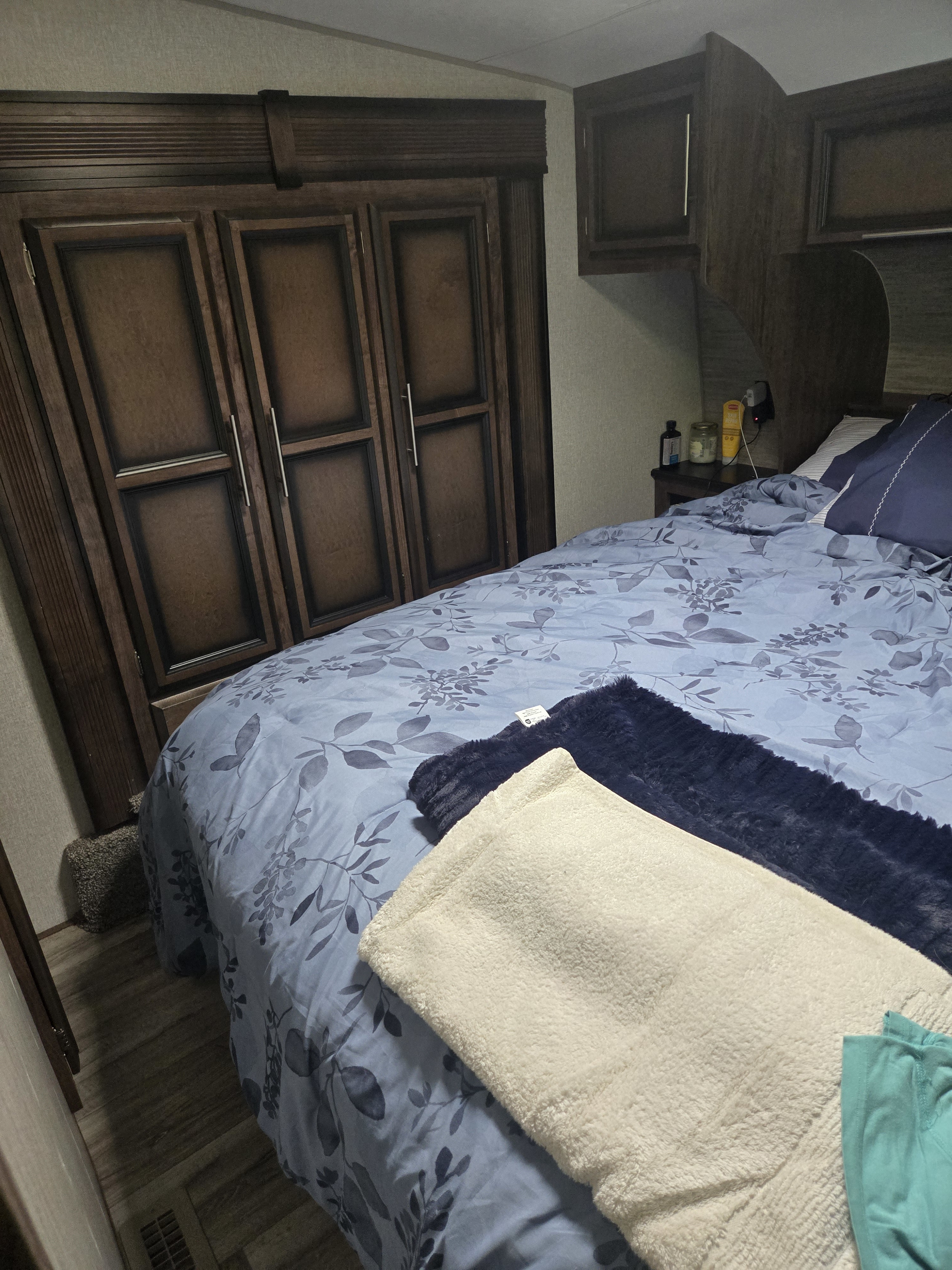 Cozy RV rental bedroom with dark wood cabinets, a blue floral bed, and soft white & navy blankets.. Durango Half-Ton 2021