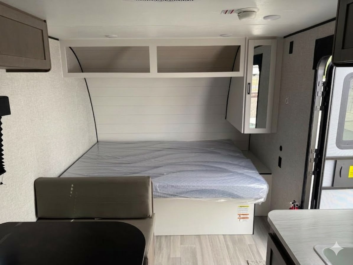 Inside a modern RV rental: a clean sleeping area with a new bed, overhead cabinets, and nearby dinette/kitchen. Ready for adventures.. Starcraft Autumn Ridge 2026