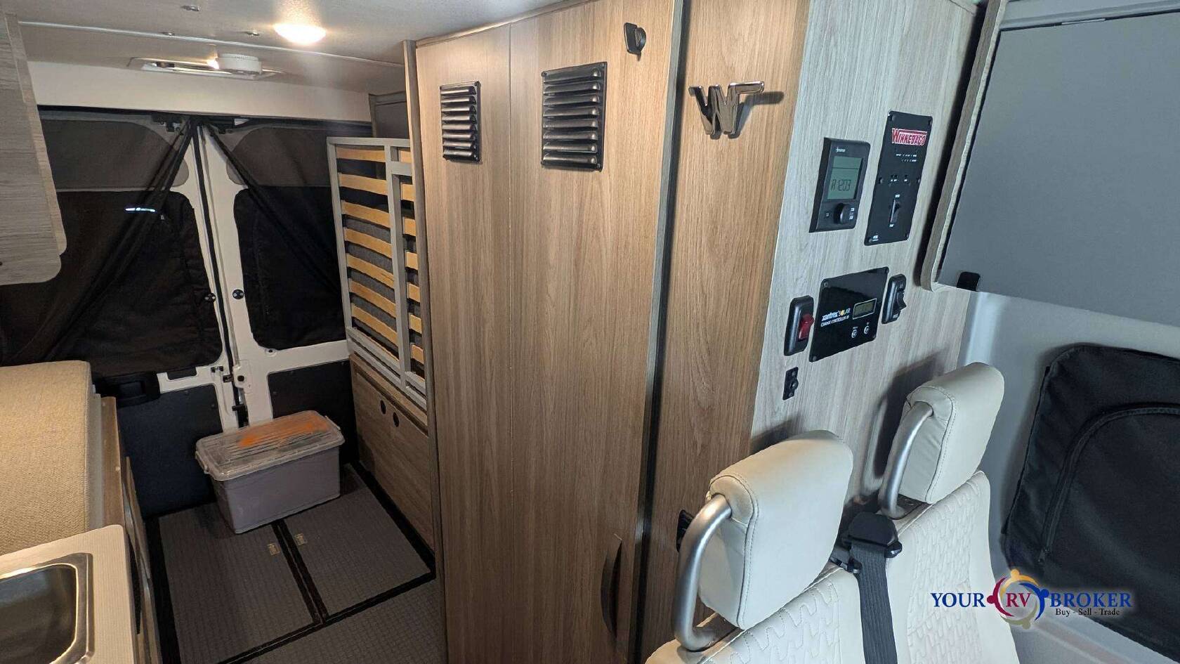 This RV rental camper van interior features a control panel, bed frame, rear screened doors, and floor storage.. Winnebago Solis Ram ProMaster 59P 2021
