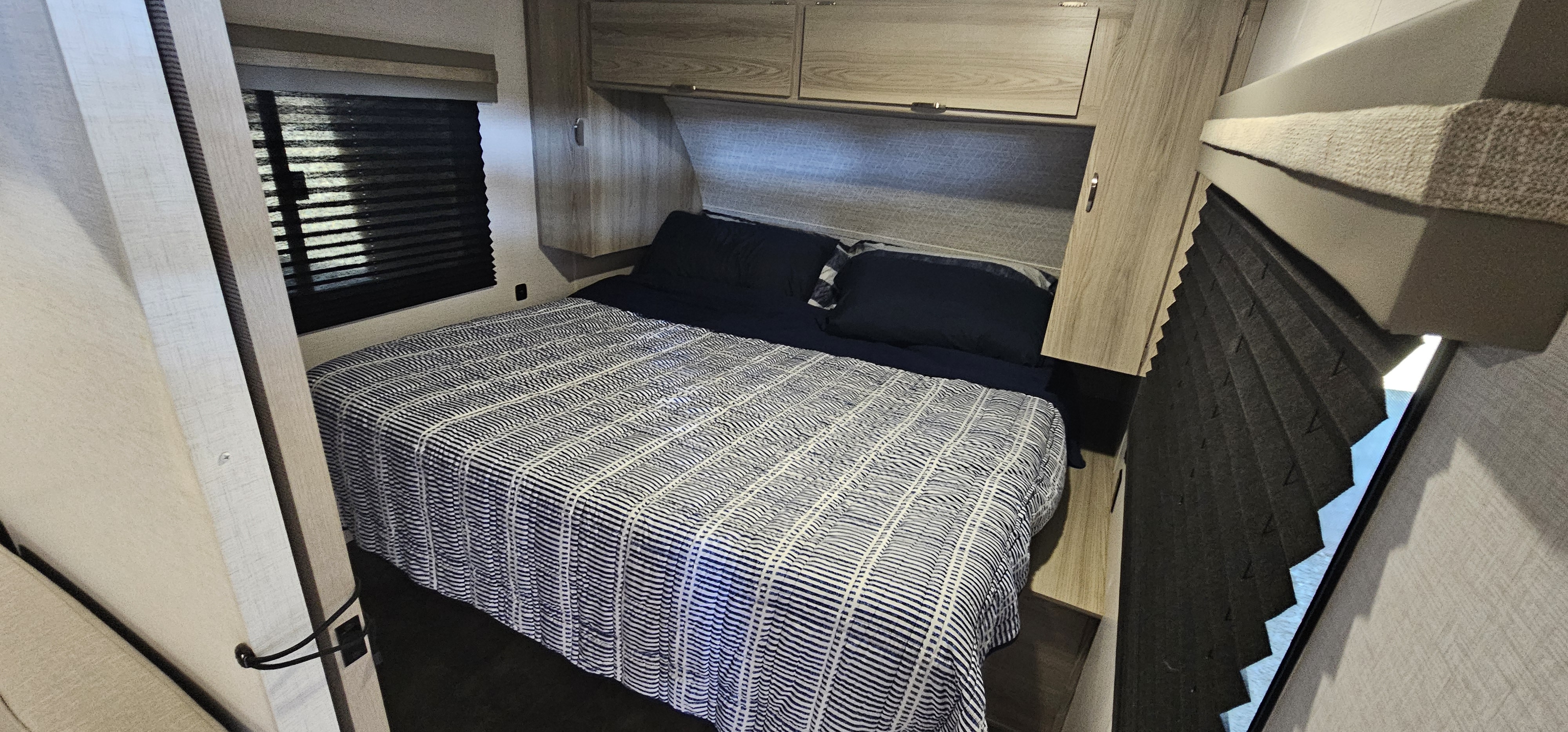 Cozy RV rental bedroom featuring a striped bed, overhead storage cabinets, and privacy blinds on both sides.. Forest River Salem FSX 2024
