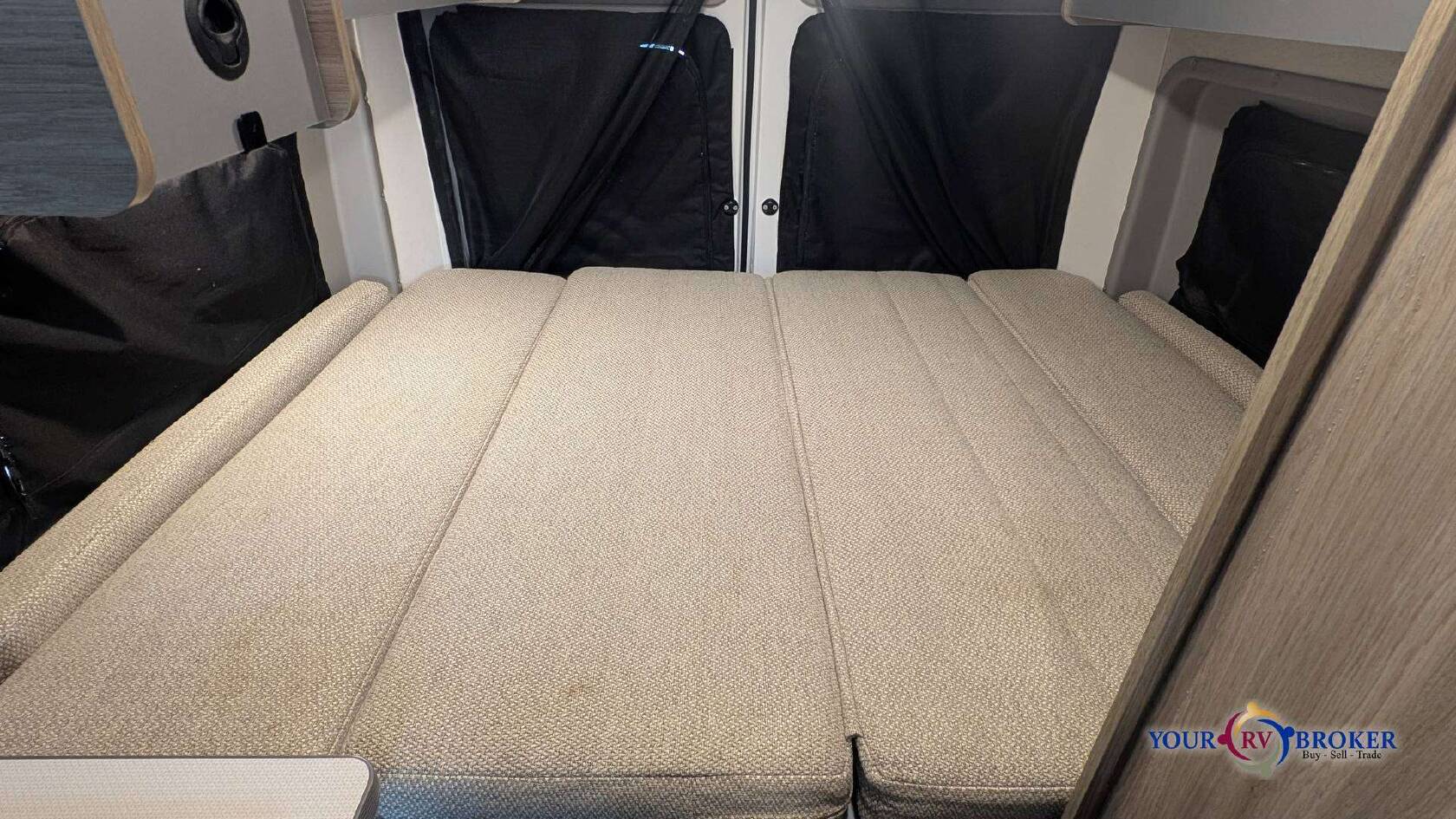This RV rental features a folded-out bed with light-colored cushions and black privacy curtains, inside a cozy camper.. Winnebago Solis Ram ProMaster 59P 2021