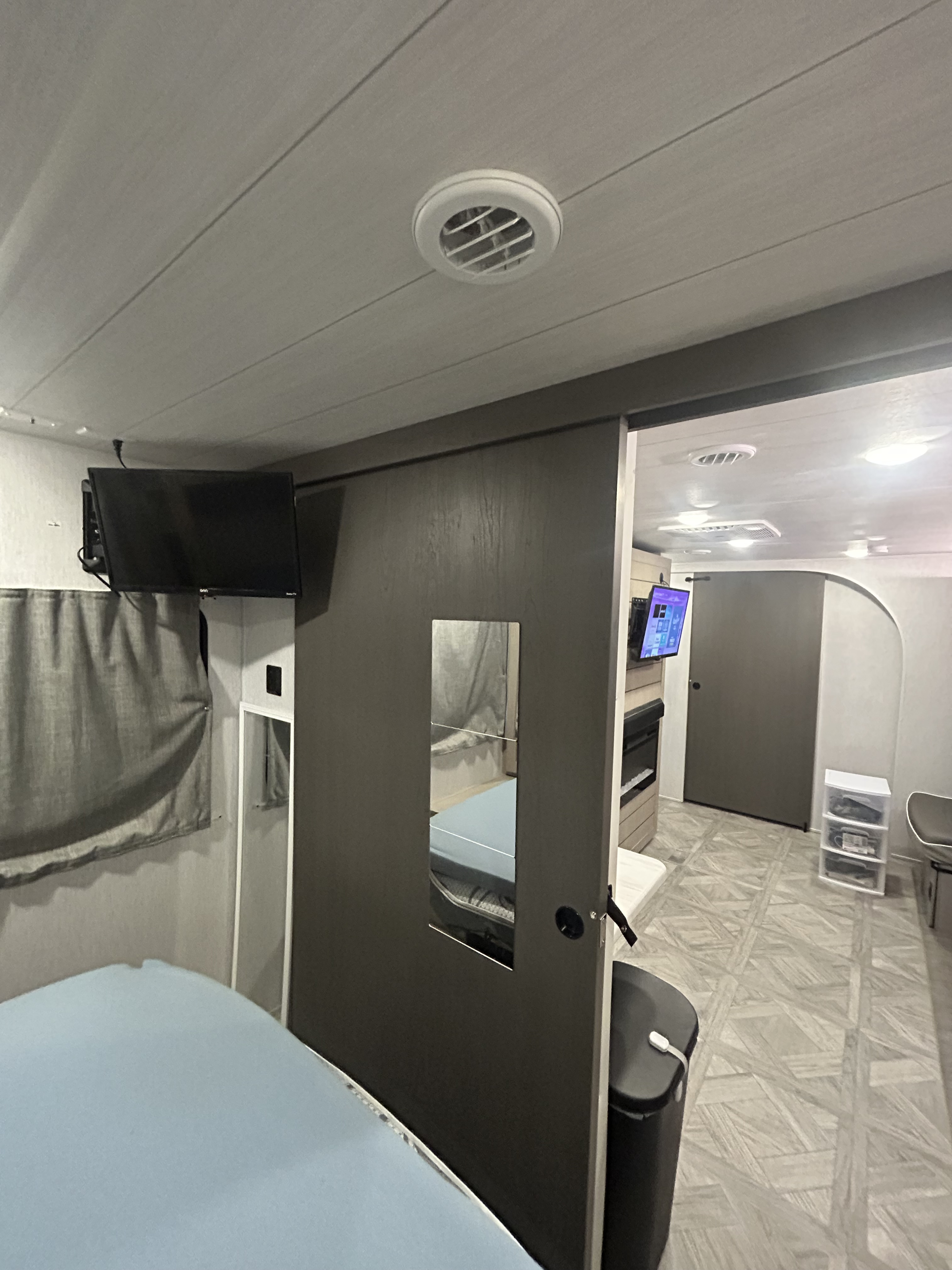 Spacious rv rental interior, showing a bedroom with TV, a sliding door, & an open living area with another TV & fireplace.. Forest River Salem Platinum 2024