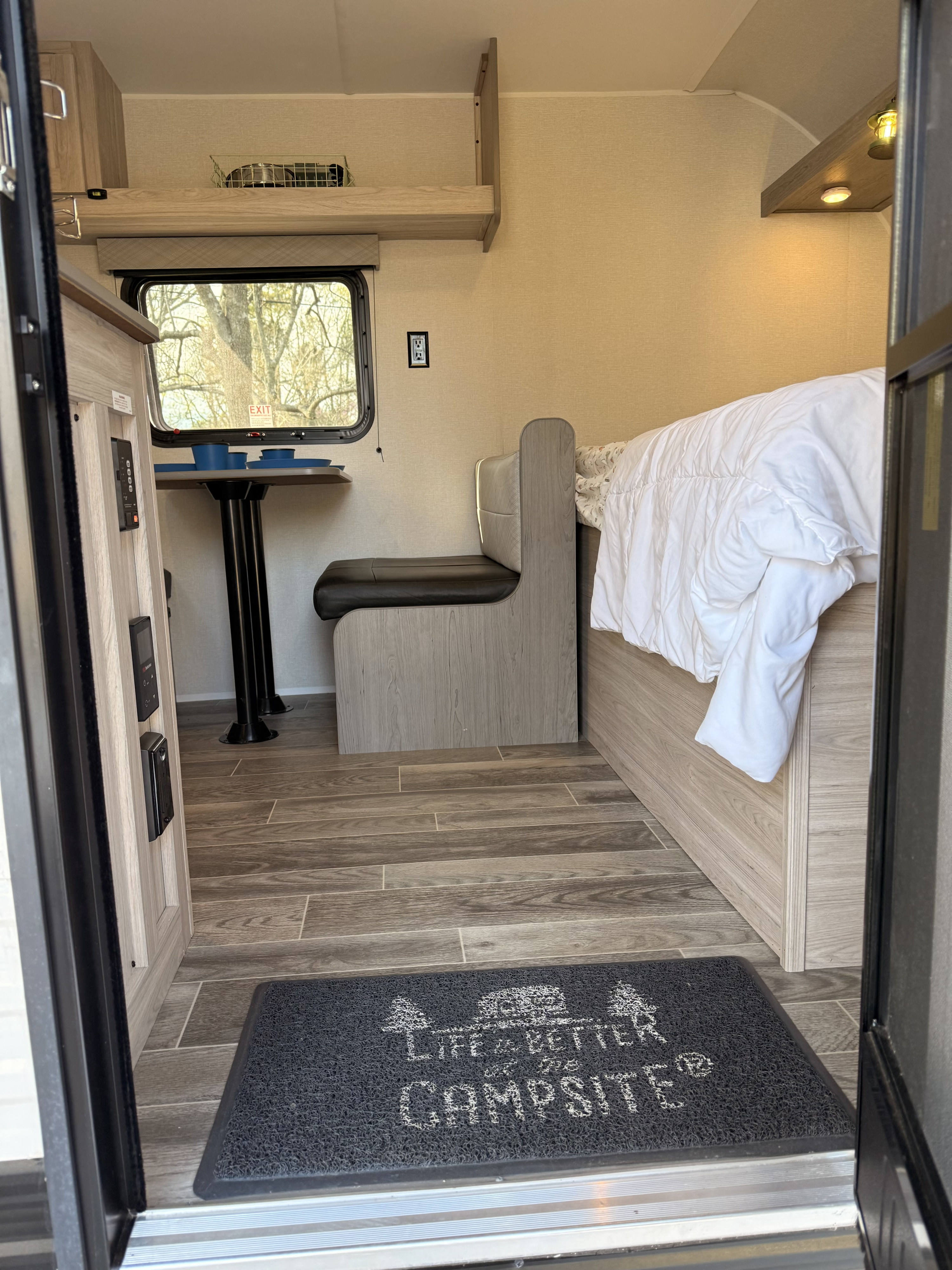 RV rental interior featuring a dinette, bed, modern light wood finishes, and a "campsite" welcome mat.. Heartland RVs Pioneer 2025