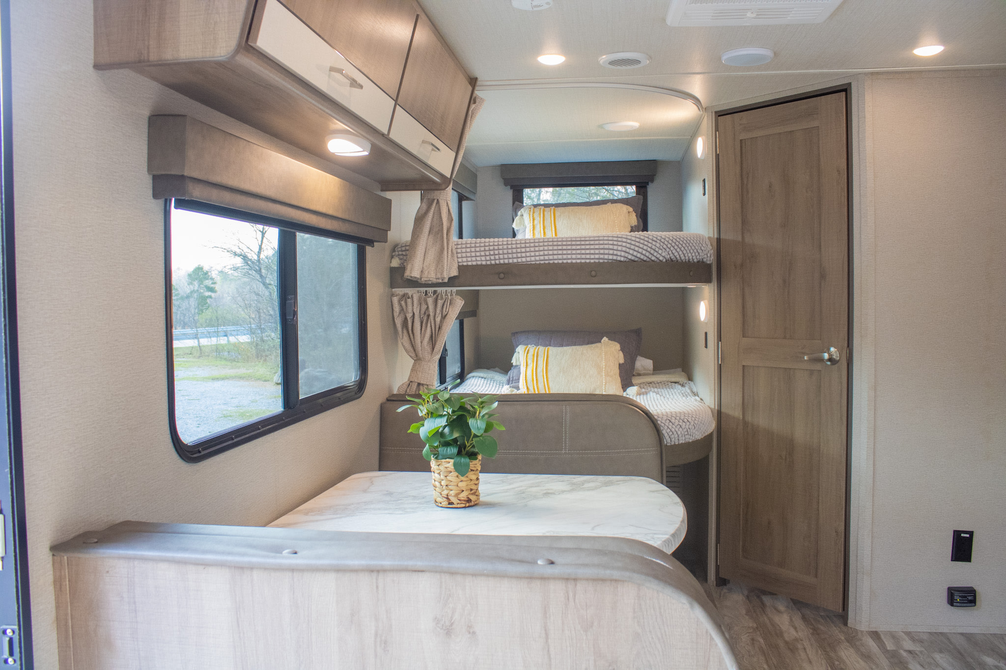 Inside an RV rental: a bright dinette with a plant, cozy bunk beds, and outdoor views for your next travel adventure.. Grand Design Imagine 2022