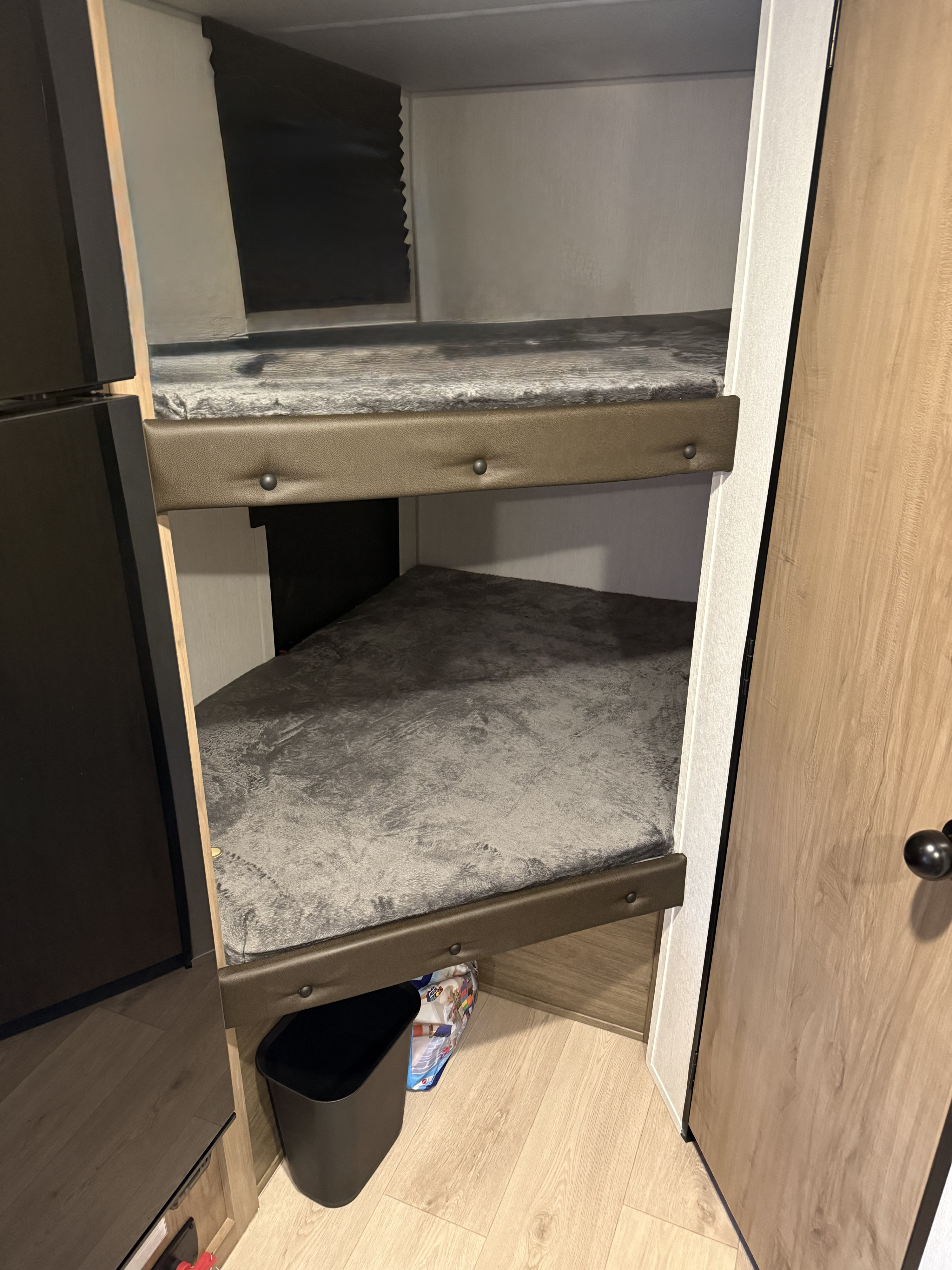 Compact bunk beds in an rv rental, featuring grey fuzzy blankets and upholstered edges. A black trash can is below.. Forest River Cherokee Wolf Pup 2025