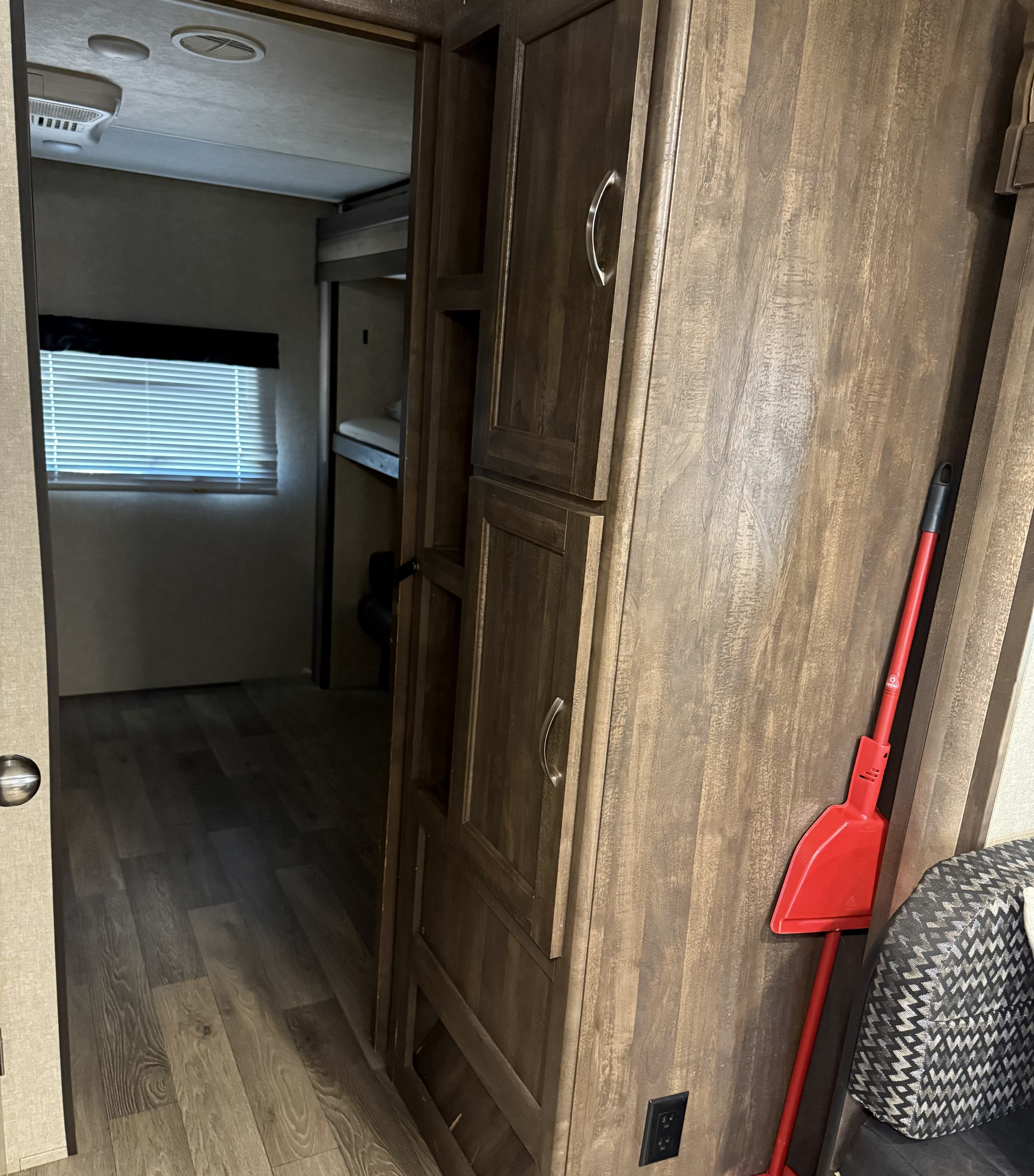 RV rental interior with dark wood-look flooring and cabinets, bunk beds, and a red broom for keeping things tidy.. Forest River Vibe Extreme Lite 2019