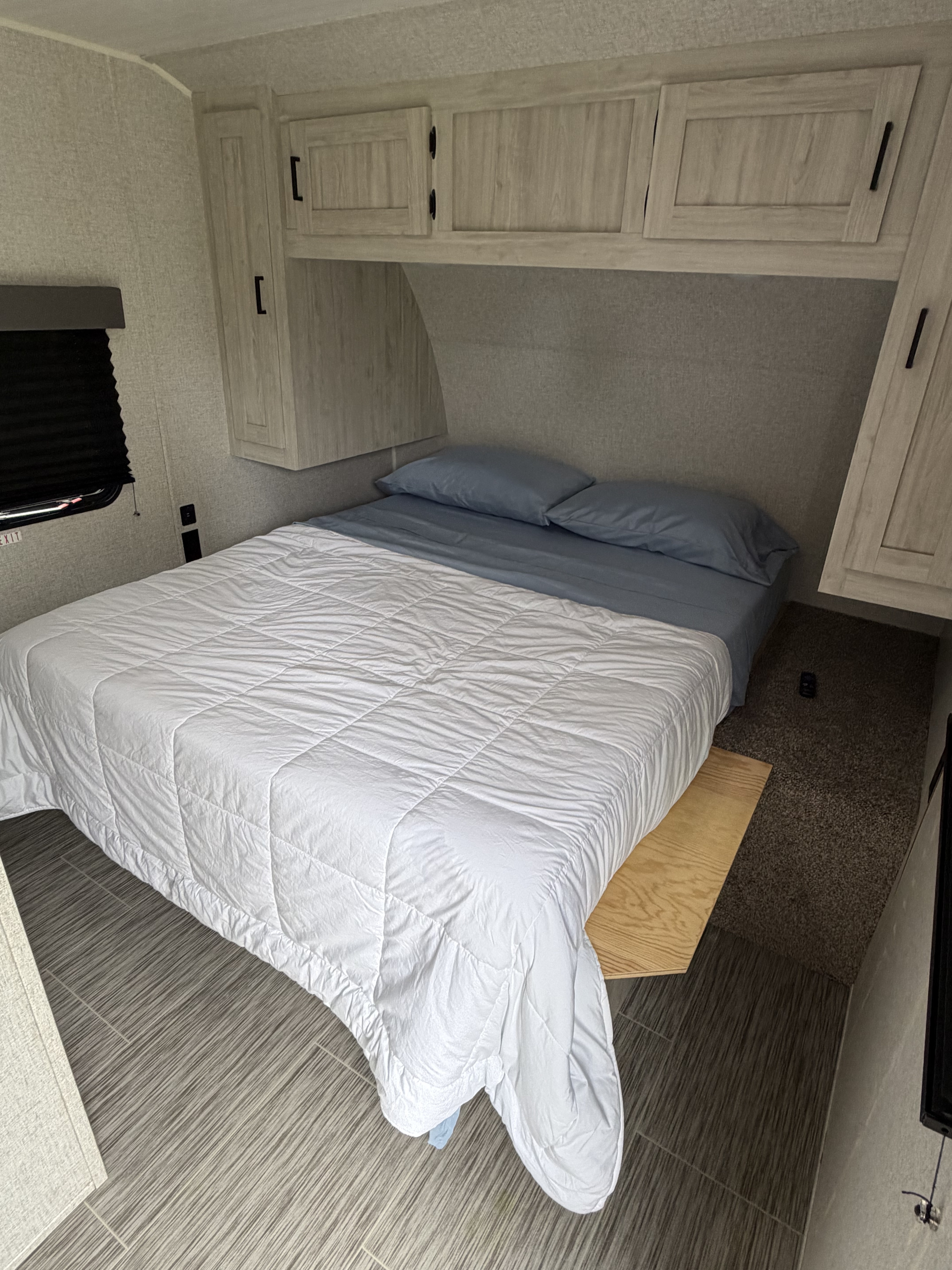 Cozy RV rental bedroom: bed with blue sheets/white comforter, light wood cabinets, textured walls, and mixed flooring.. East to West Silver Lake 2023