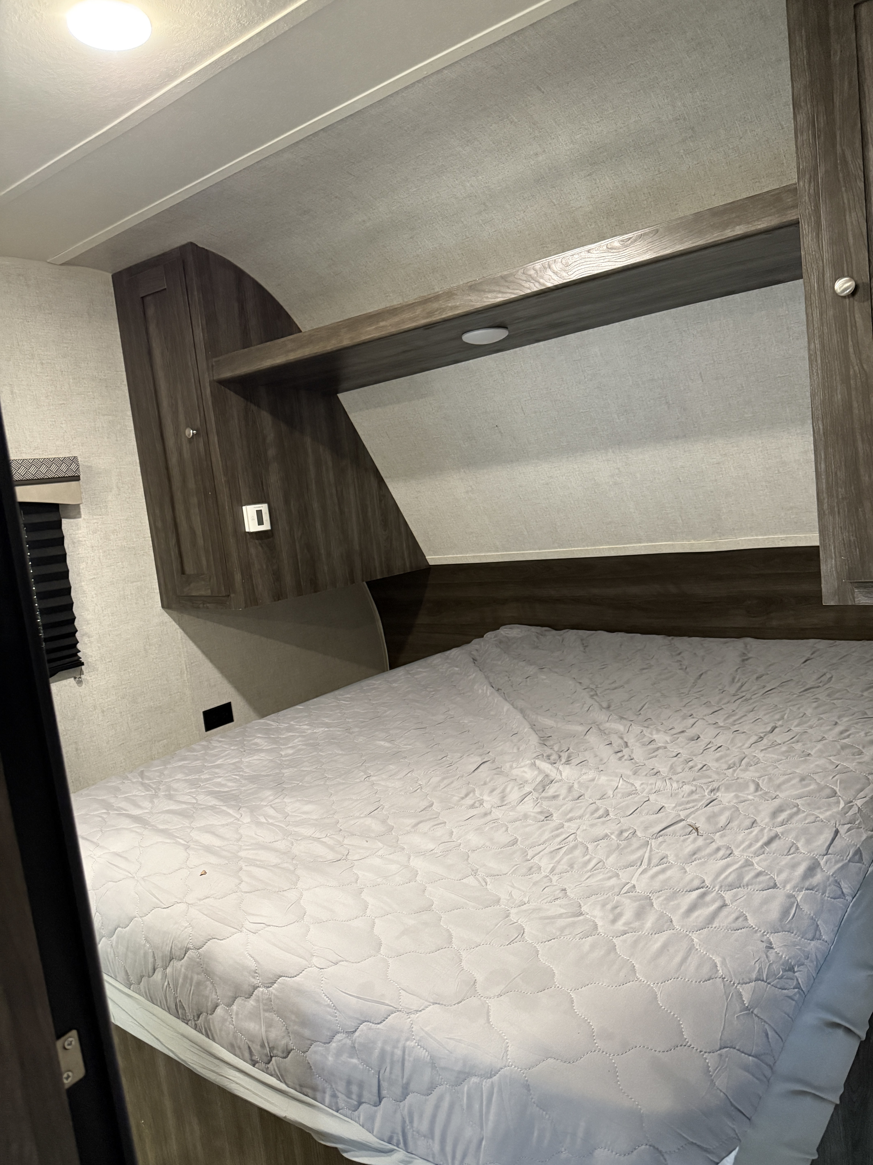 RV rental bedroom interior shows a comfortable bed with a quilted cover, dark wood overhead storage, and a ceiling light.. Starcraft Autumn Ridge Outfitter 2019