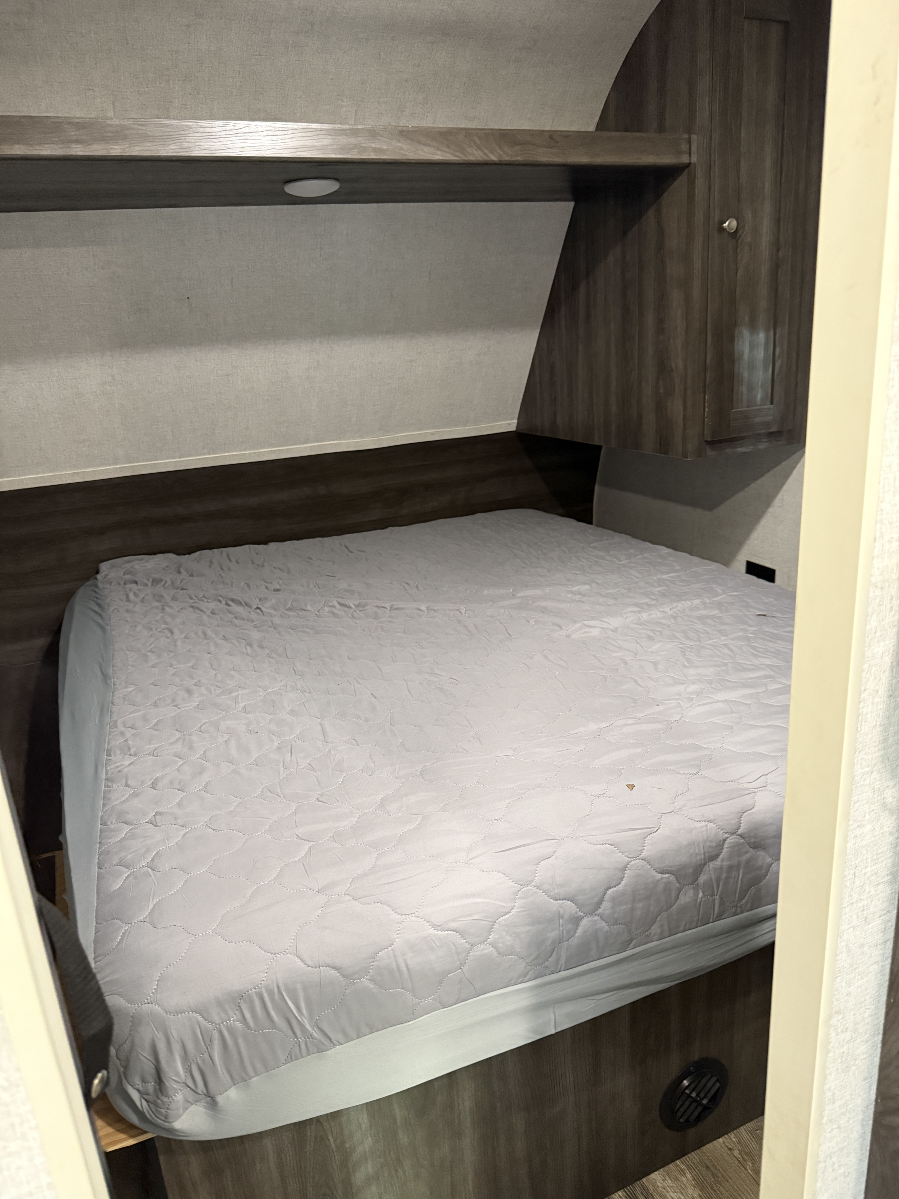 Cozy RV rental sleeping area with a quilted bed, overhead shelf, light, and wood paneling. Perfect for travel comfort.. Starcraft Autumn Ridge Outfitter 2019
