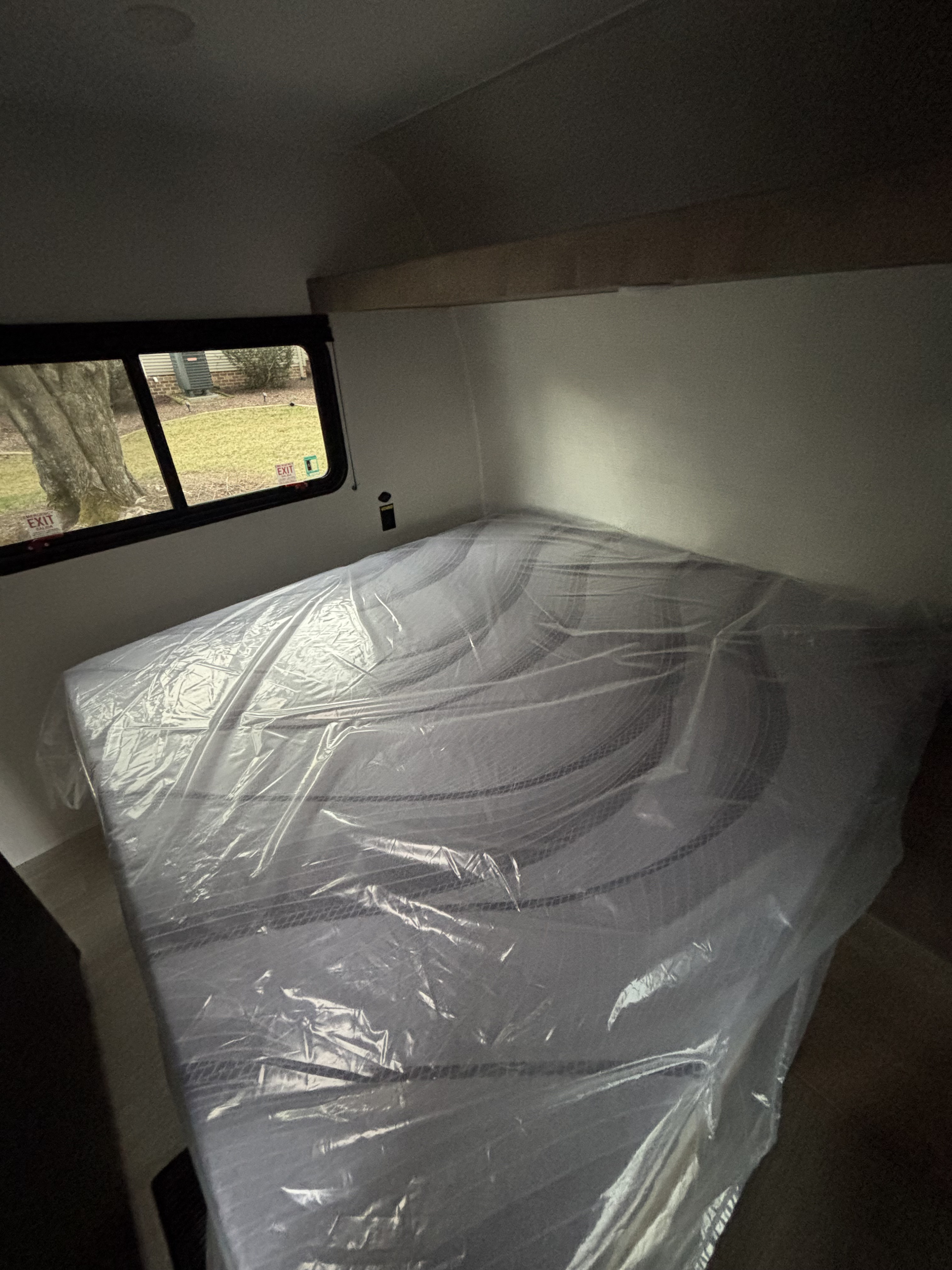 RV rental bedroom with a new, plastic-covered mattress and an outdoor view through the window.. Keystone Springdale 261BHC 2026