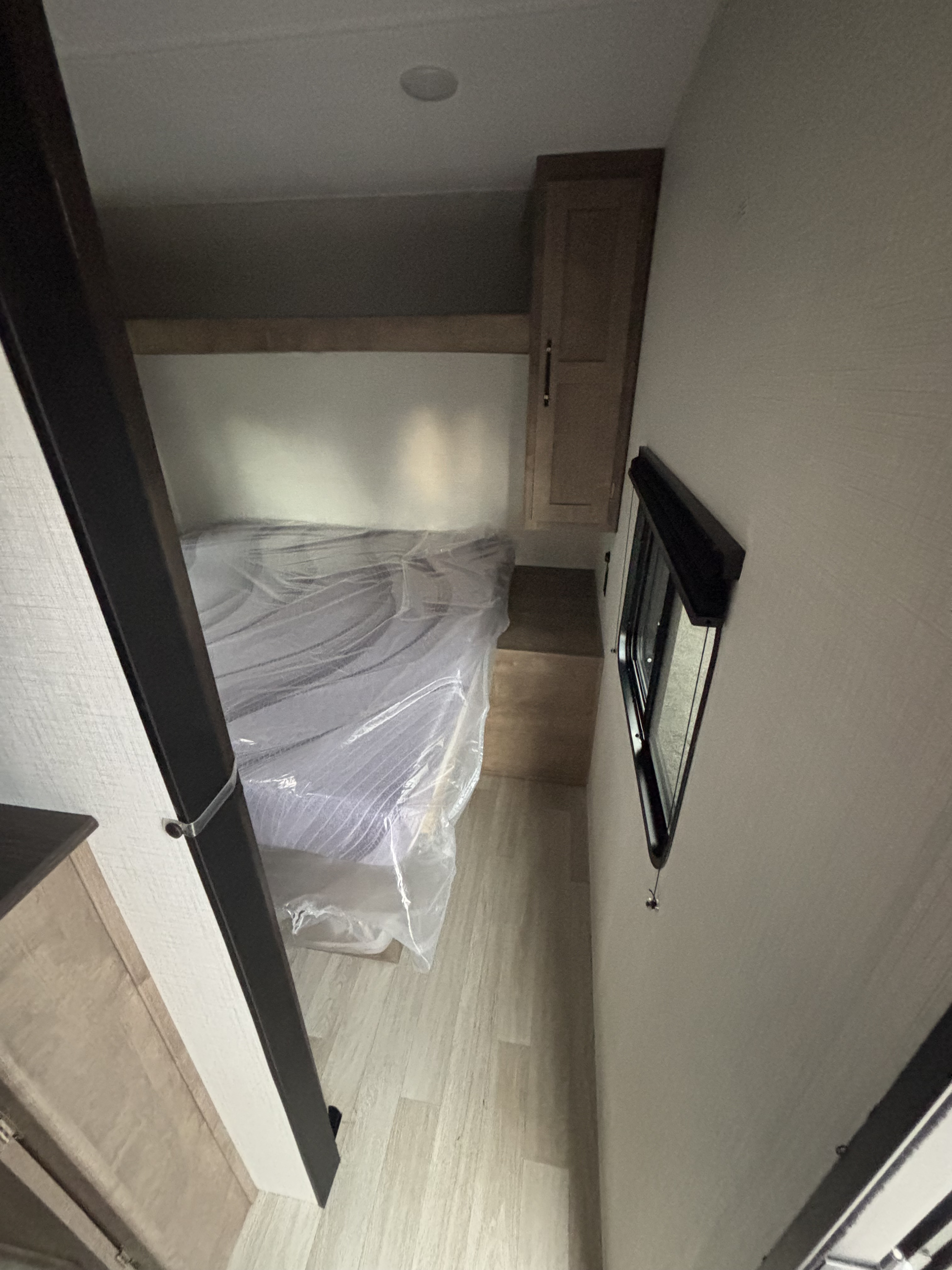 Cozy RV rental bedroom with a plastic-covered bed, built-in cabinets, and a window with a blind. Perfect for compact living.. Keystone Springdale 261BHC 2026