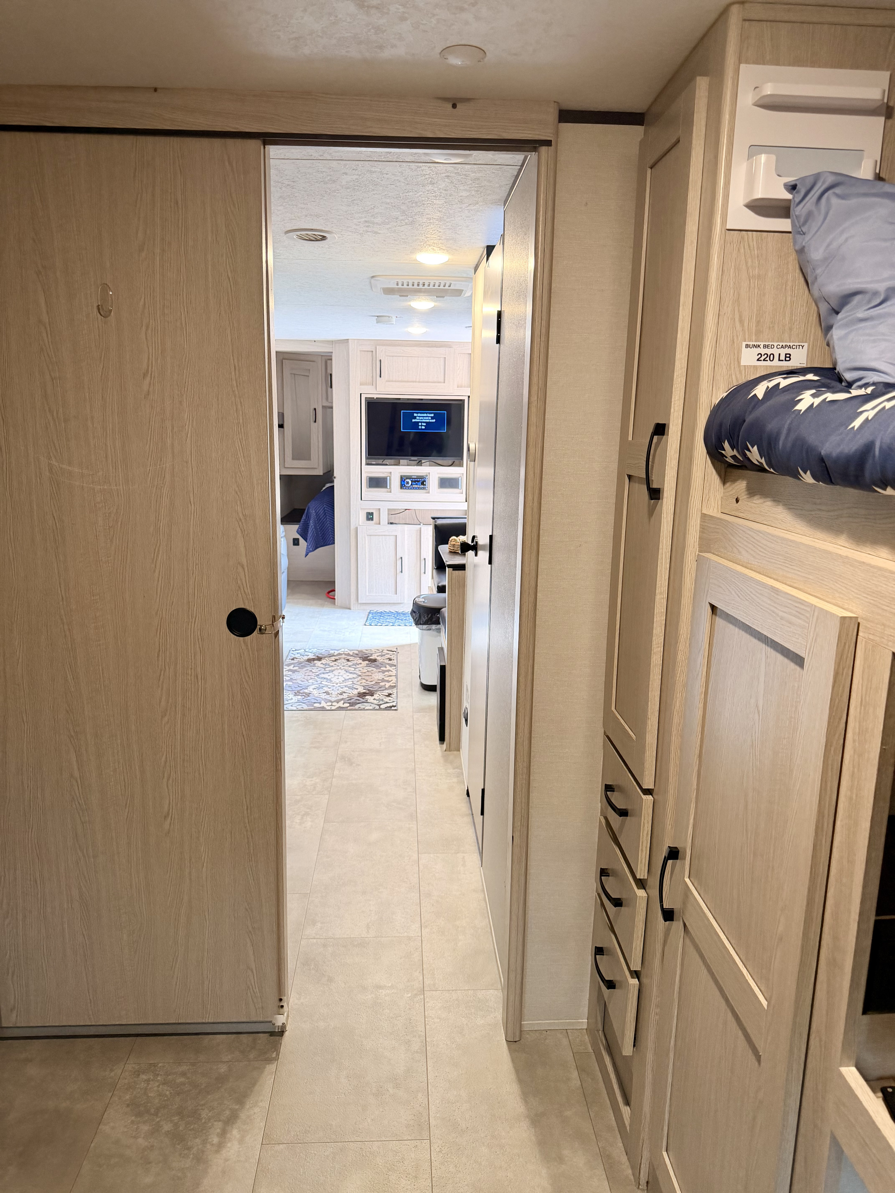 RV rental interior: A hallway with light wood cabinets, bunk beds, and a peek into the modern kitchen/living area.. Coachmen Apex 2021