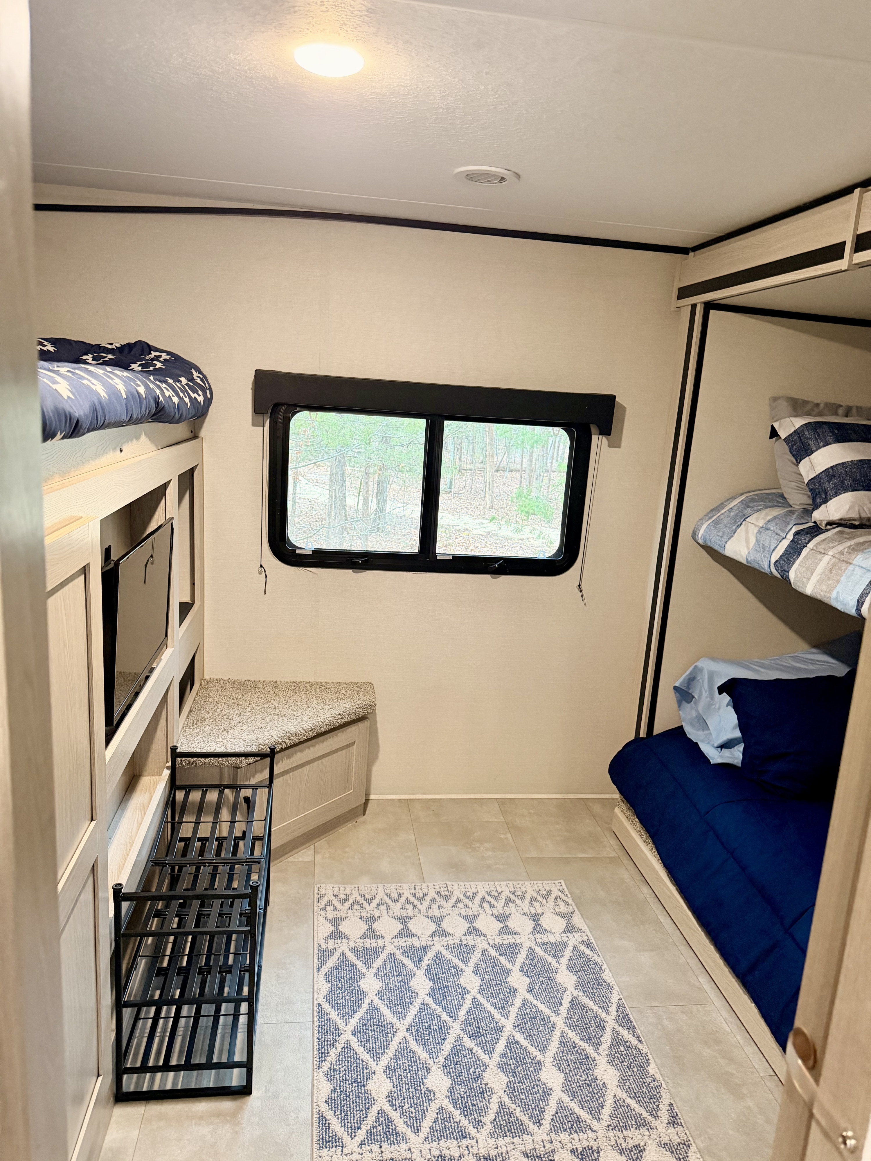 This RV rental bunk room features two sets of bunk beds, a window view, TV, bench, and shoe rack on a tiled floor.. Coachmen Apex 2021