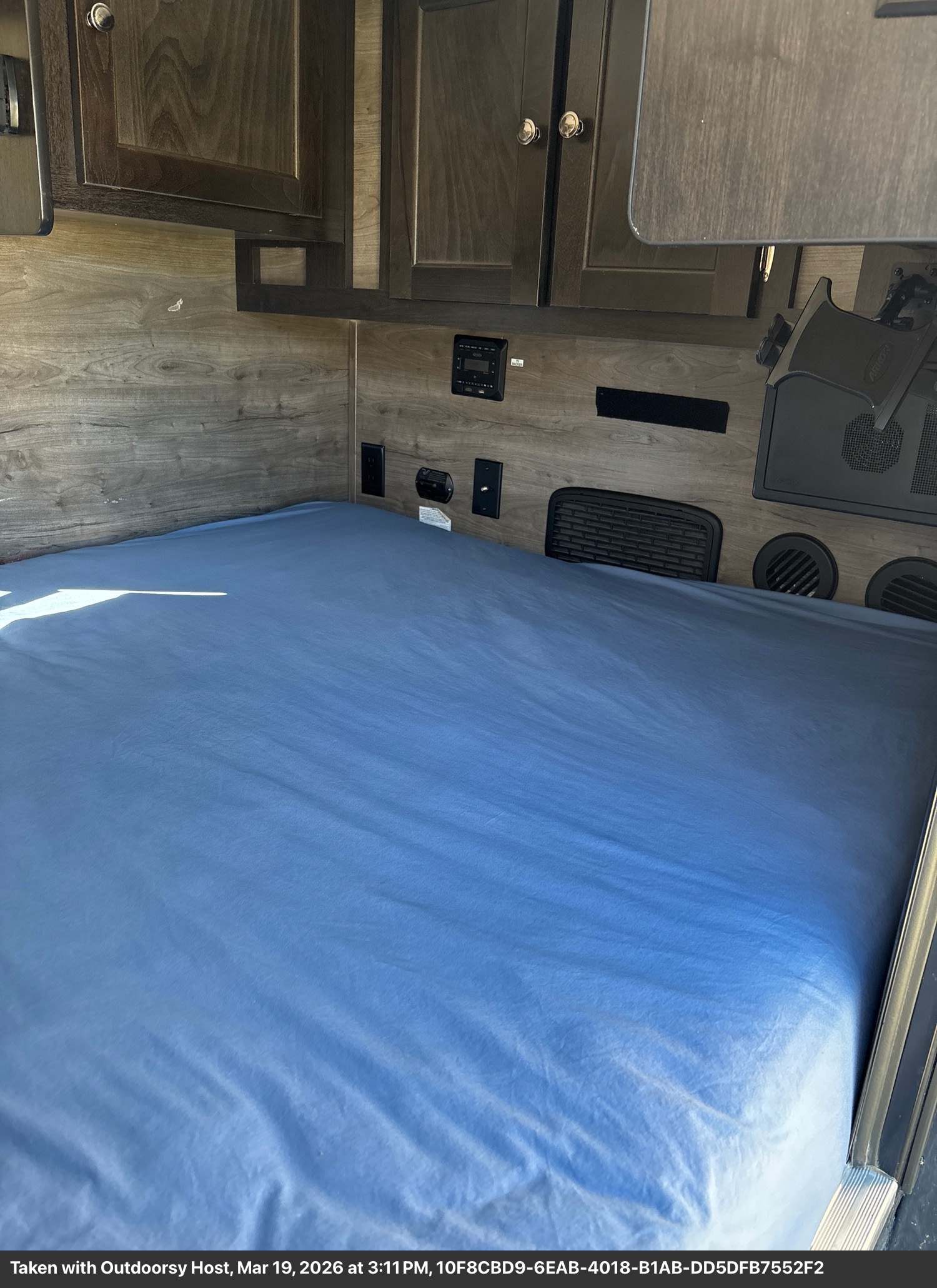 Inside this RV rental: a cozy bedroom with a blue bed, wood walls, overhead cabinets, and built-in amenities.. Braxton Creek Free Solo 2022