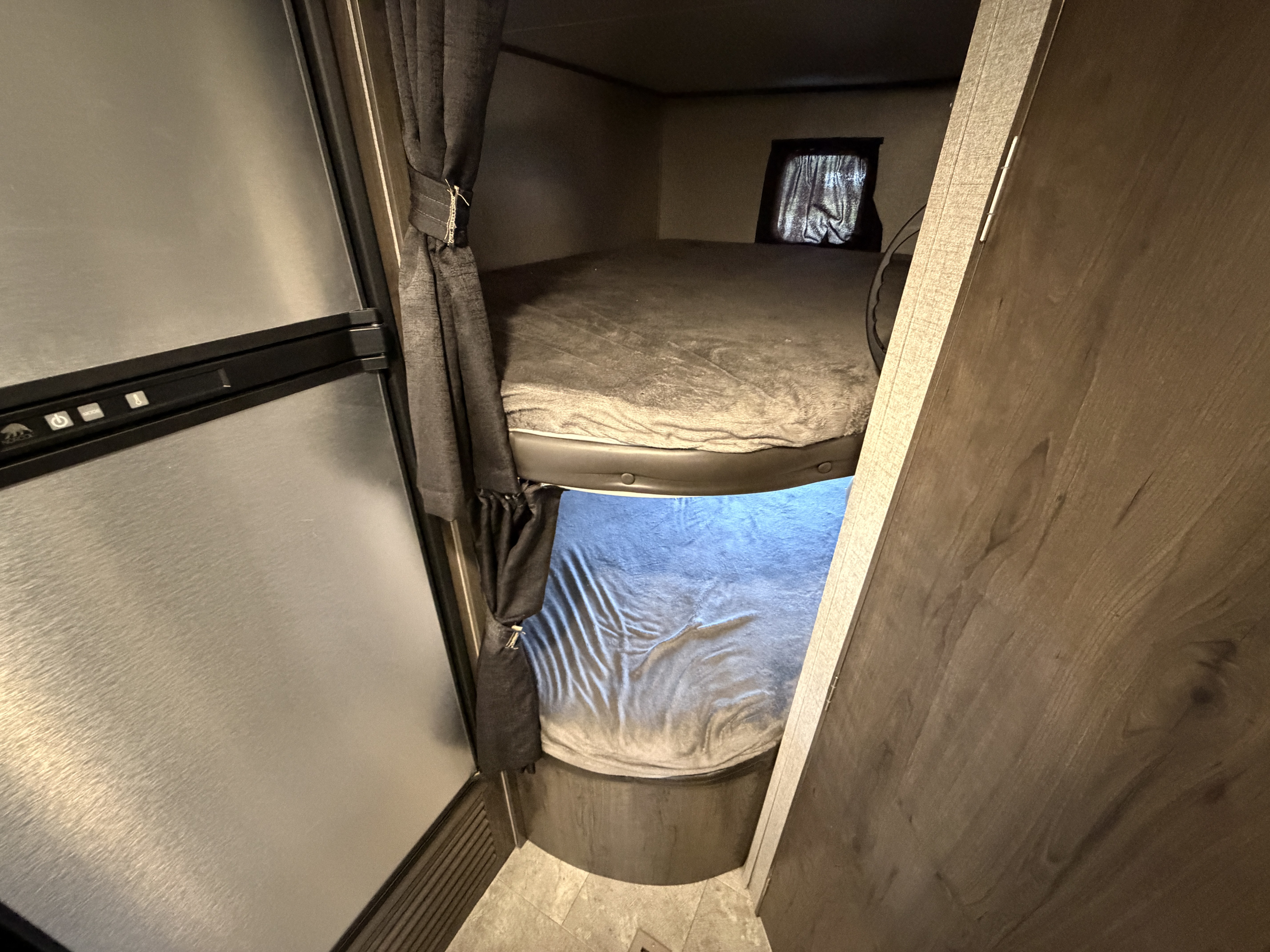 Interior of an RV rental: two cozy bunk beds with privacy curtains, beside a stainless steel refrigerator.. Jayco Jay Flight SLX 2020