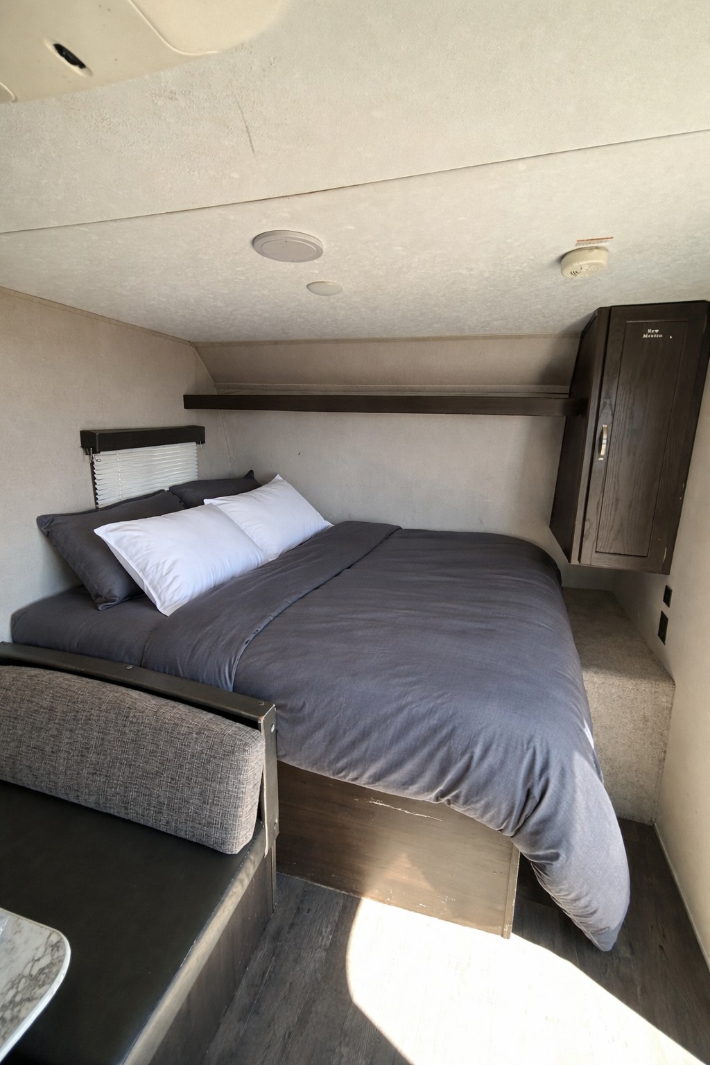 This cozy rv rental bedroom features a neatly made dark grey bed, white pillows, a window, and wood storage cabinet.. Keystone RV Springdale 2019