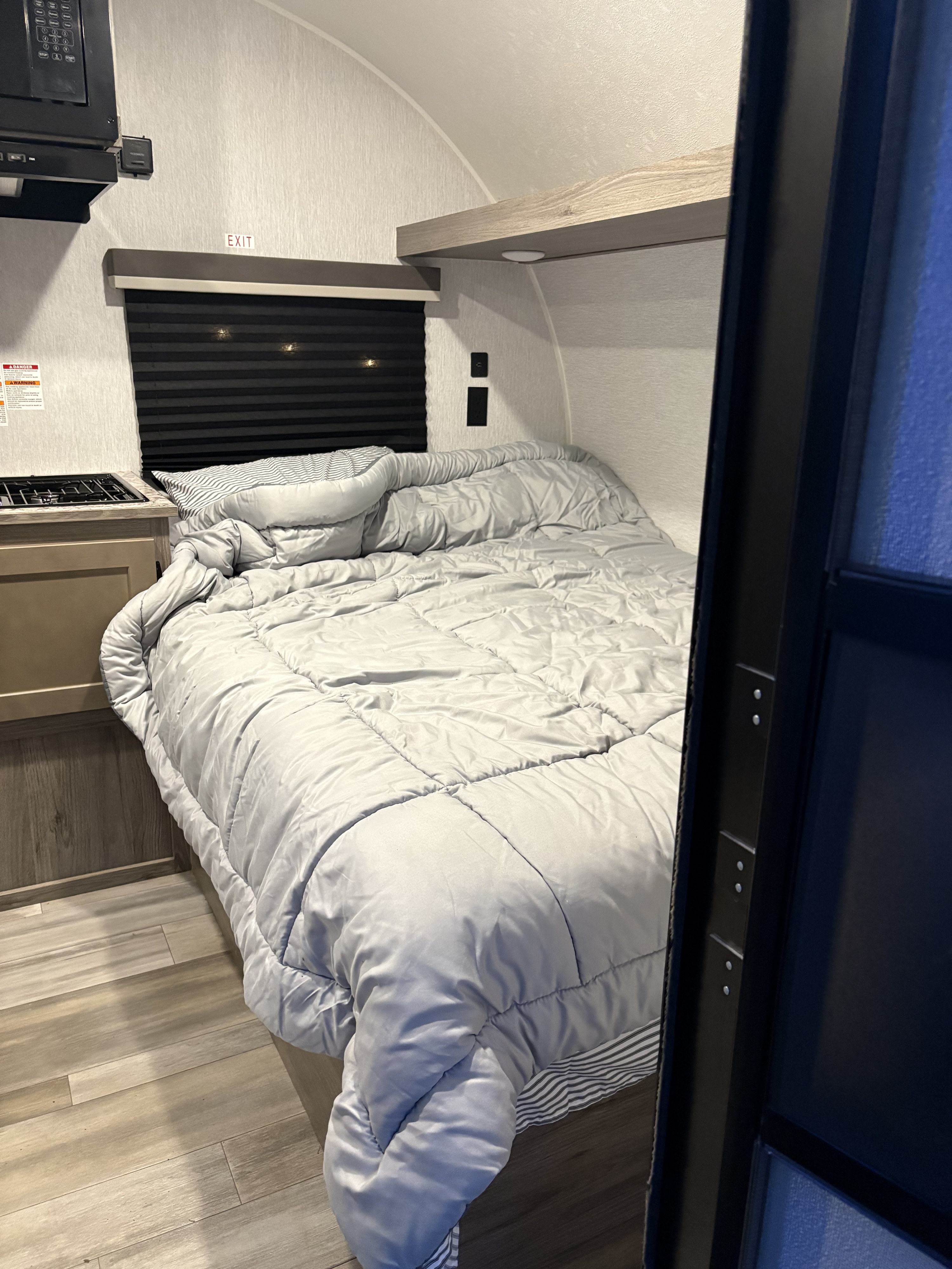 RV rental interior: A compact bedroom with a grey bedspread, small kitchen counter, stove, microwave, and wood flooring.. Sunset Park RV Sun Lite LTD 2025