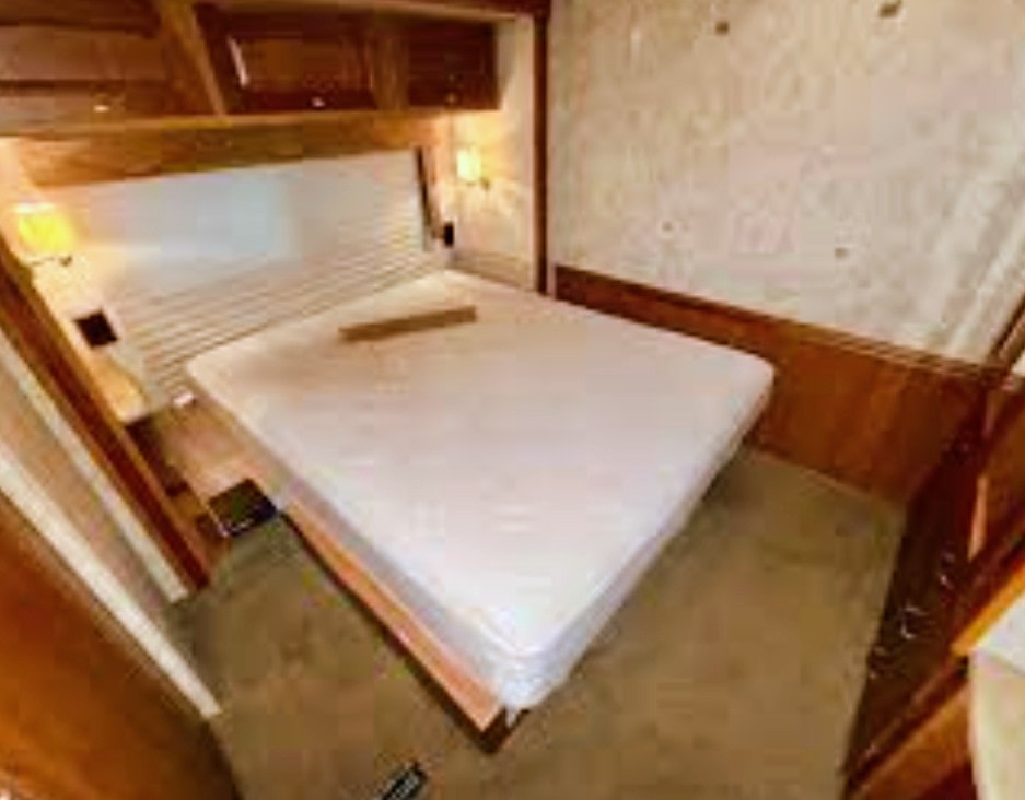 This RV rental bedroom offers a comfortable bed with a white mattress, slatted headboard, and warm wood finishes.. Winnebago Sightseer 2010