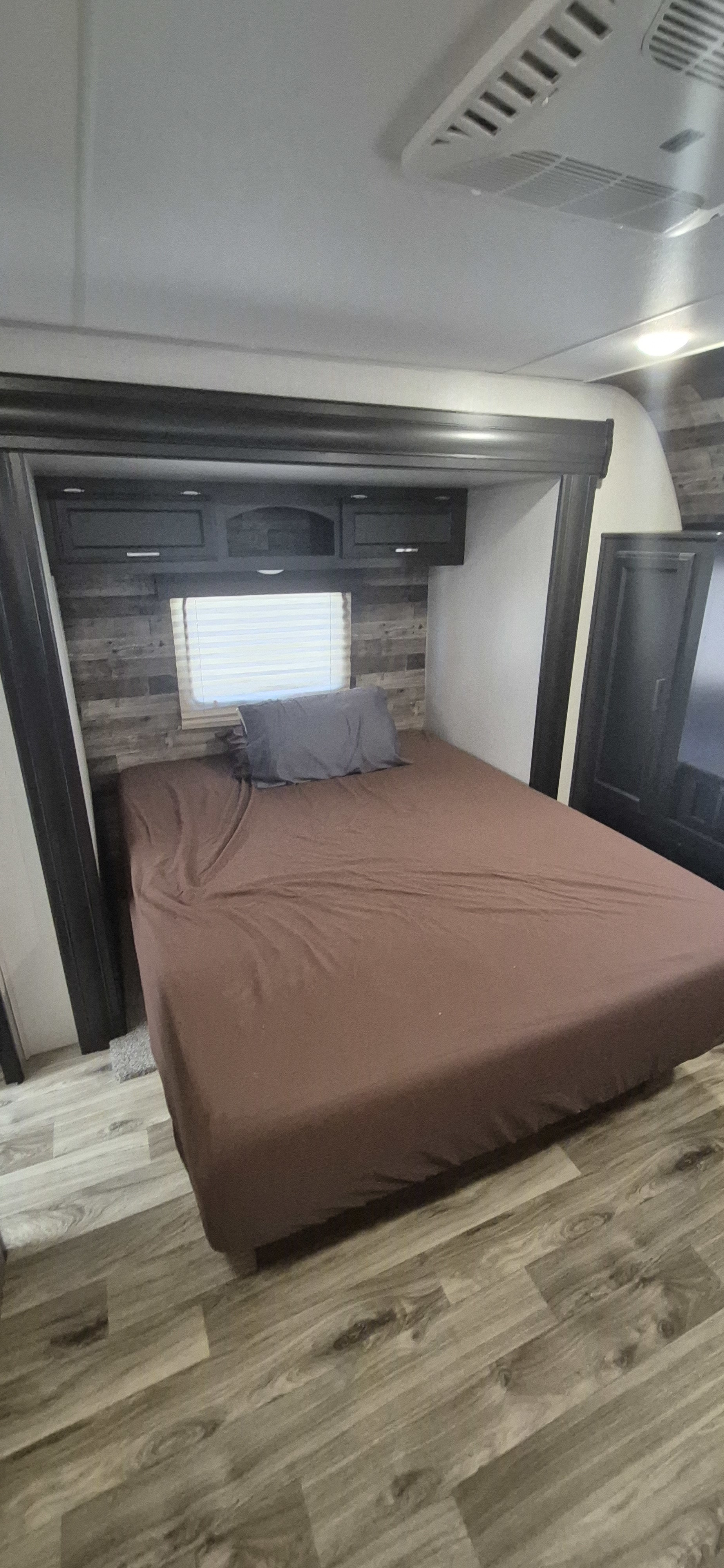 Cozy RV rental bedroom showing a bed, overhead storage, and window, with wood-look flooring and textured wall paneling.. Venture Venture Trailer 2019