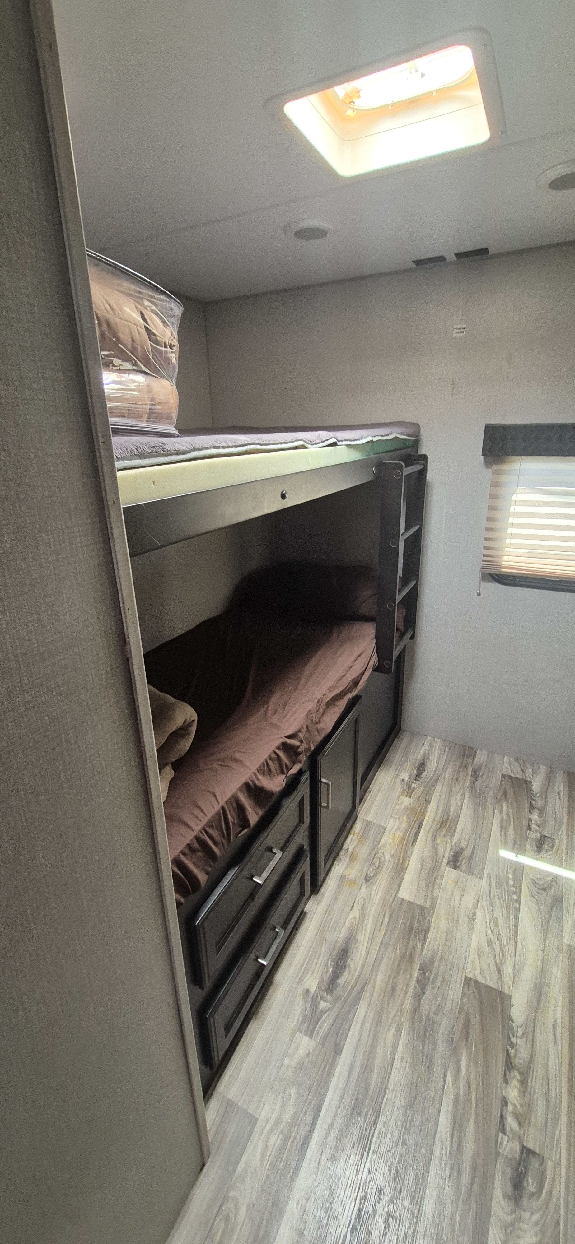 Inside an RV rental: bunk beds with bedding, built-in storage drawers, a window, and wood-look flooring for cozy stays.. Venture Venture Trailer 2019