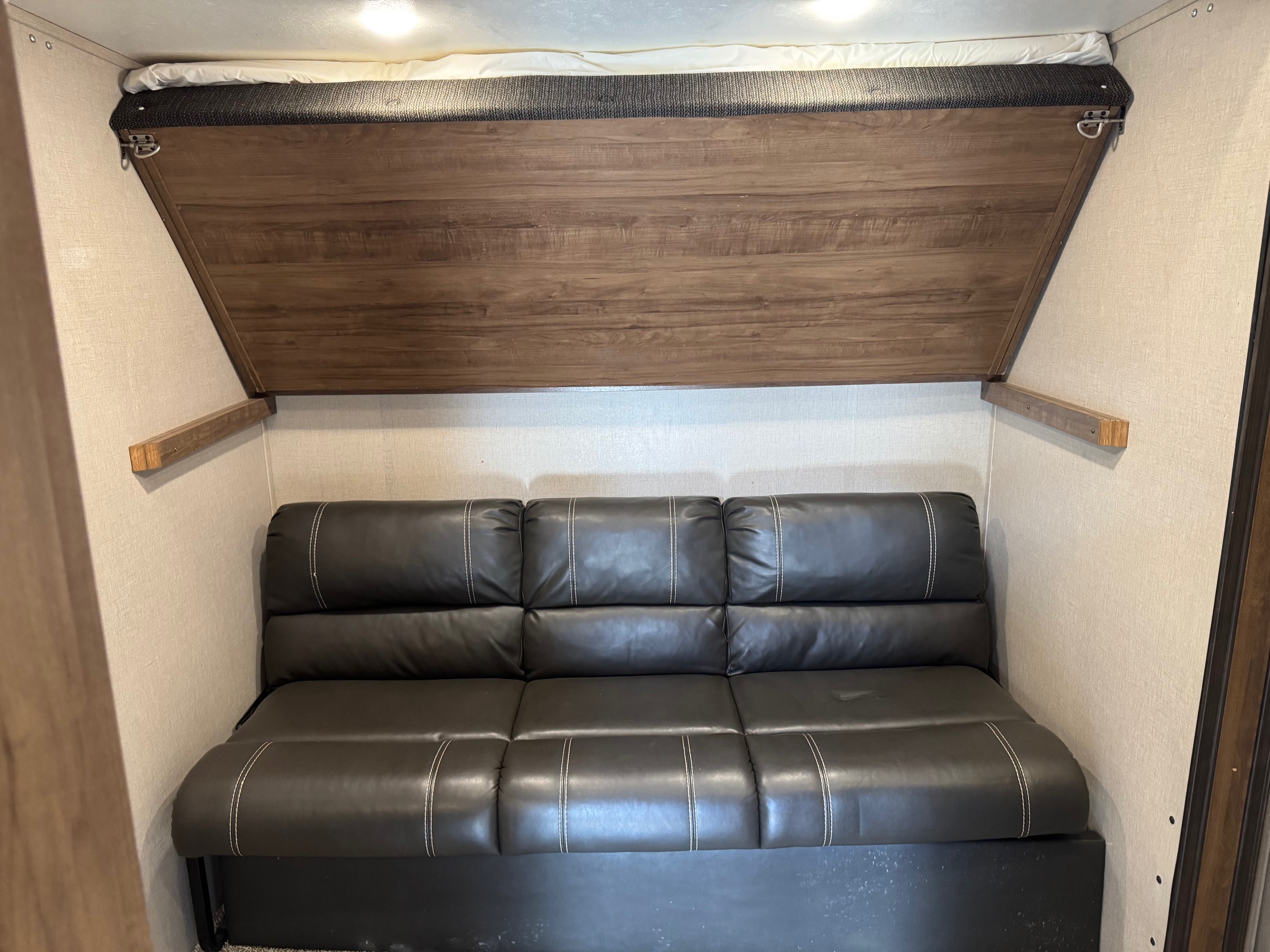 Inside an rv rental, a dark leather sofa sits below a pull-down wooden bunk bed, offering versatile sleeping and seating in a compact space.. Forest River Coachmen Chaparral 2020