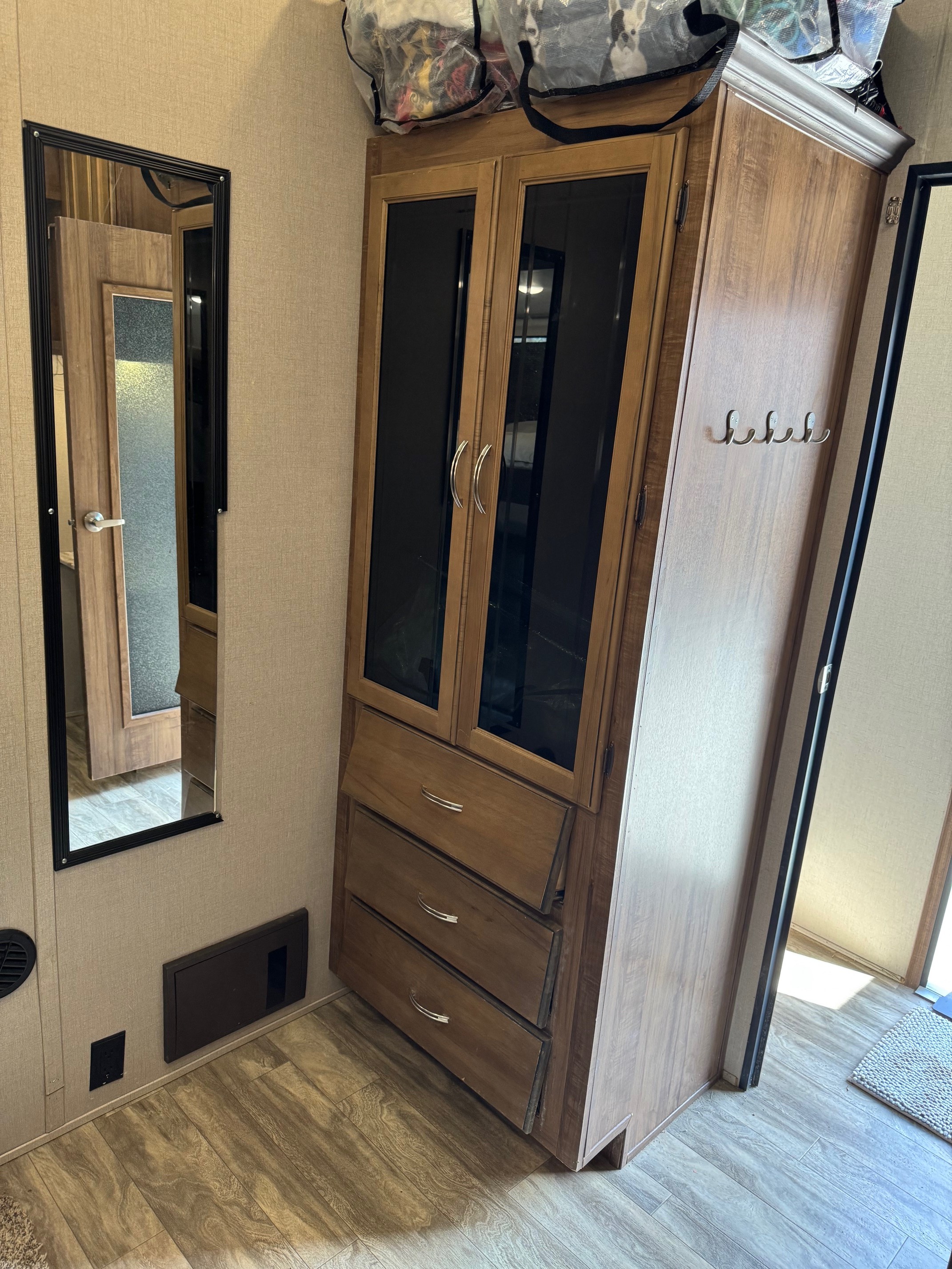 Functional RV rental interior: wood-look cabinet with glass doors, drawers, wall mirror, and coat hooks for ample storage.. Forest River Coachmen Chaparral 2020