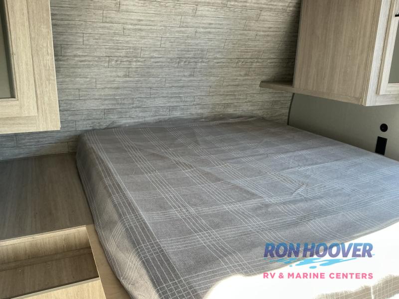 RV rental interior featuring a cozy bedroom with a grey plaid bed, wood-paneled walls, and built-in storage.. Coachmen Catalina 2025