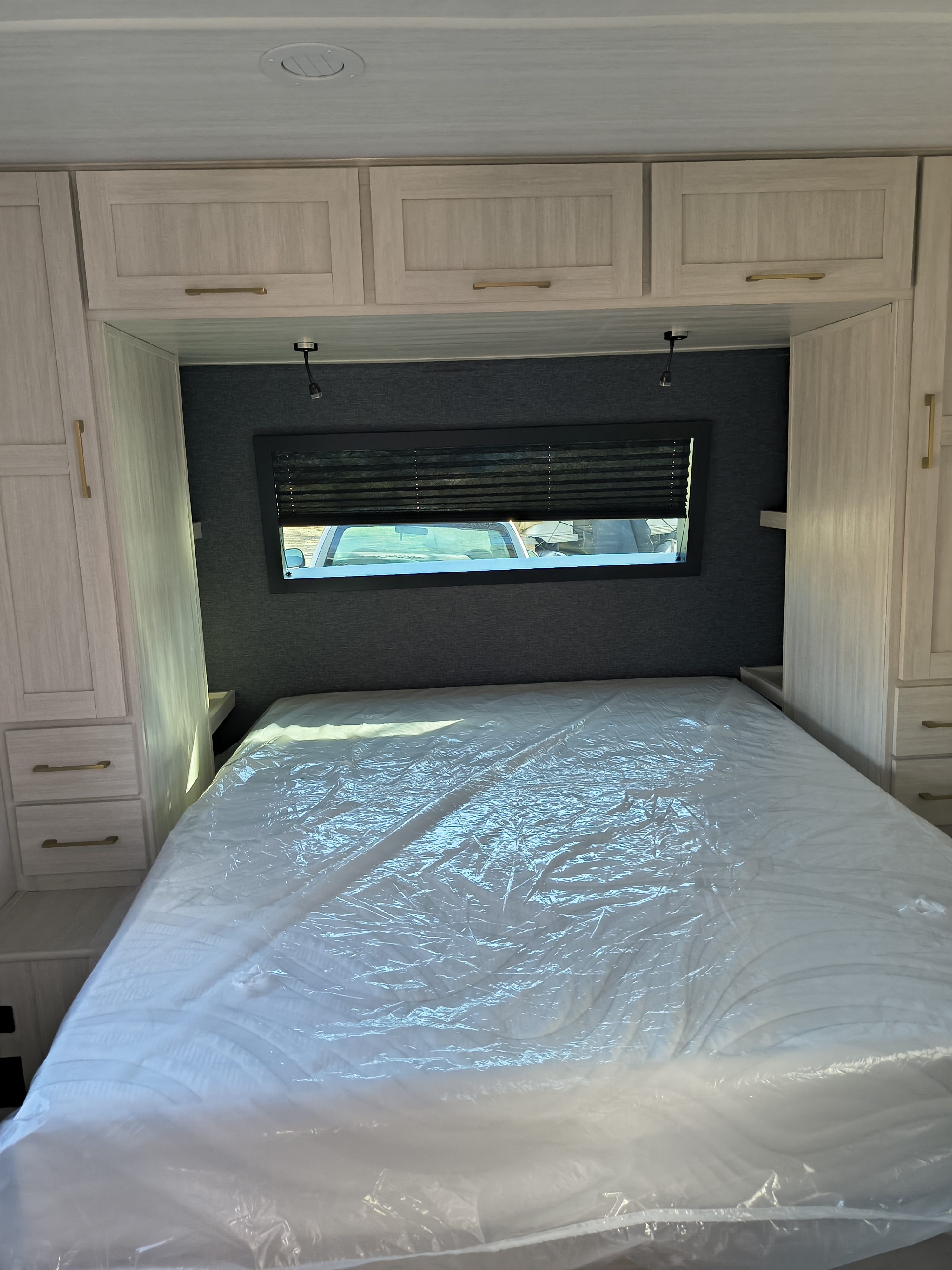 RV rental bedroom with light wood cabinets, a dark accent wall, and a bed featuring a plastic-wrapped mattress.. Forest River Surveyor Legend 2024