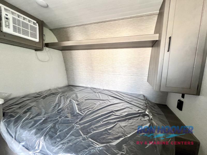 Clean RV rental bedroom with a covered bed, wall-mounted AC, and overhead storage, ready for your trip.. Keystone RV Hideout Sport 2025