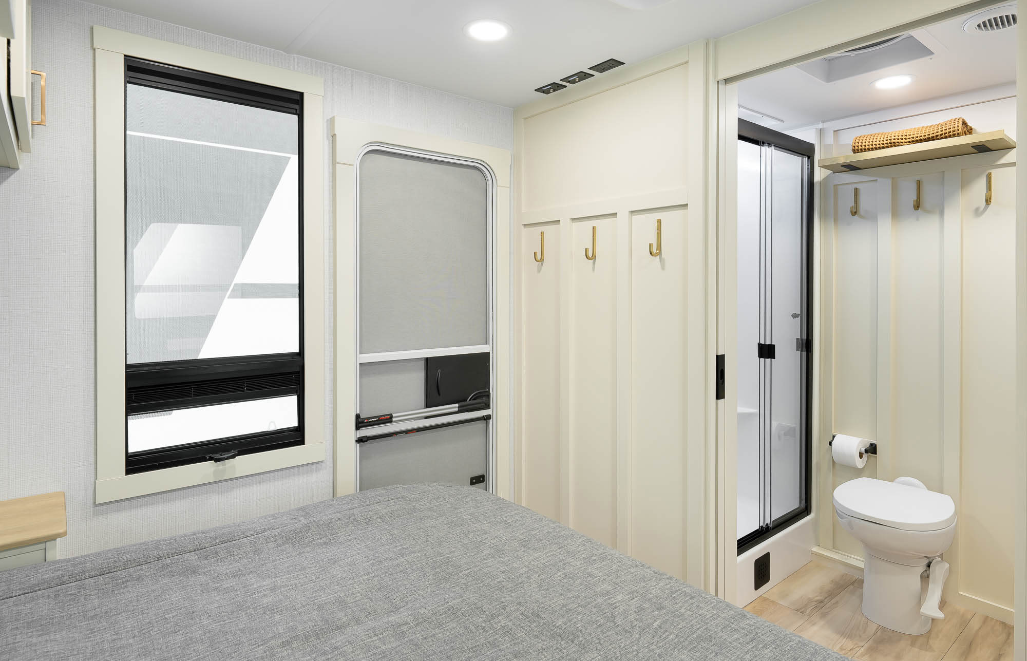 Modern RV rental interior with a cozy bedroom, window, door, and a compact bathroom featuring a toilet and shower.. Brinkley RV Model I 2026