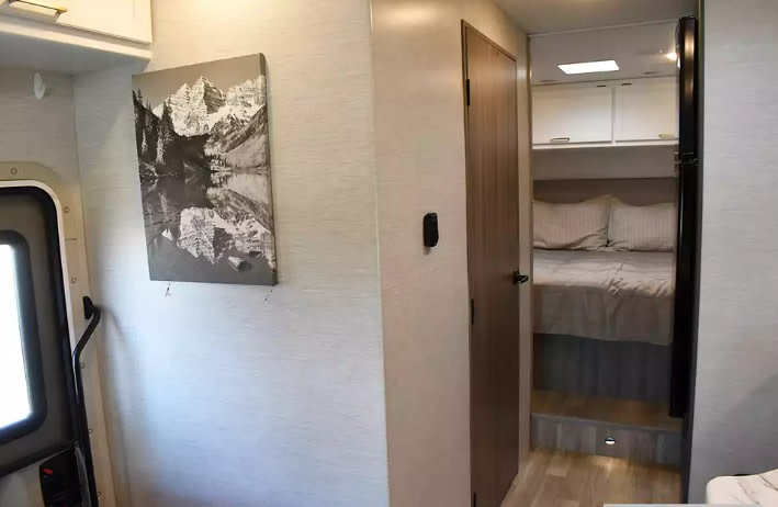 Cozy rv rental interior showing a bedroom with bed & cabinets, a hallway, and mountain artwork on the wall.. Thor Eddie Bauer 2025
