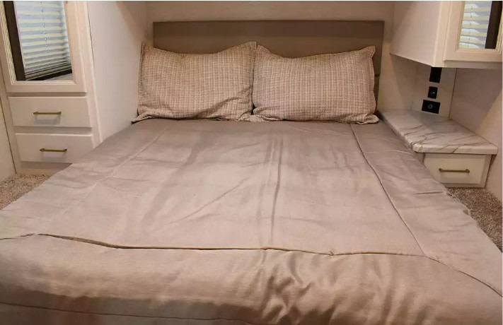 Cozy RV rental bedroom with a bed, patterned pillows, mirrored cabinet, and nightstand featuring charging outlets.. Thor Eddie Bauer 2025