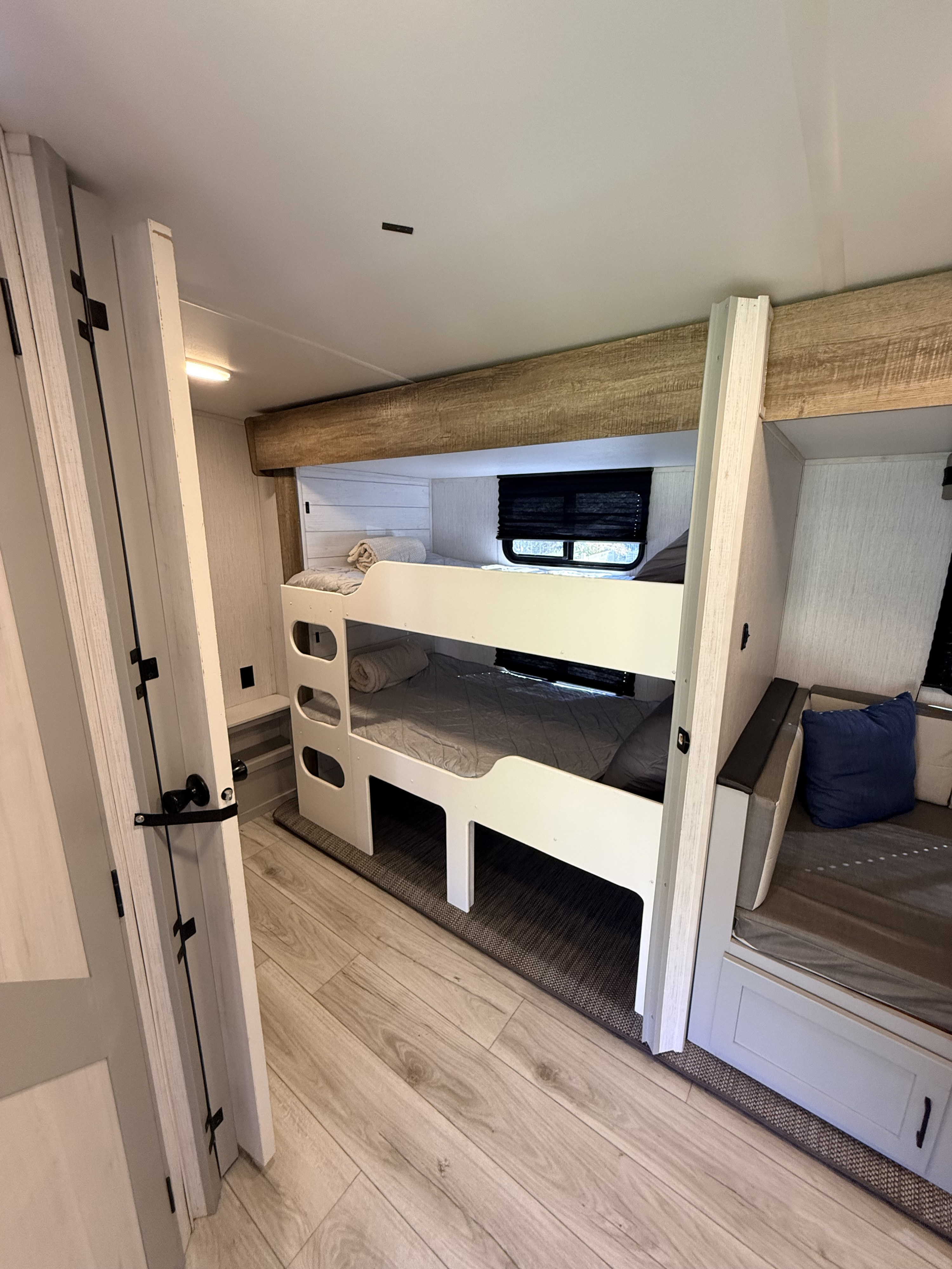This inviting RV rental interior features comfortable white bunk beds, a cozy sitting area, and wood-look flooring, ideal for family travel.. Heartland RVs North Trail 2023