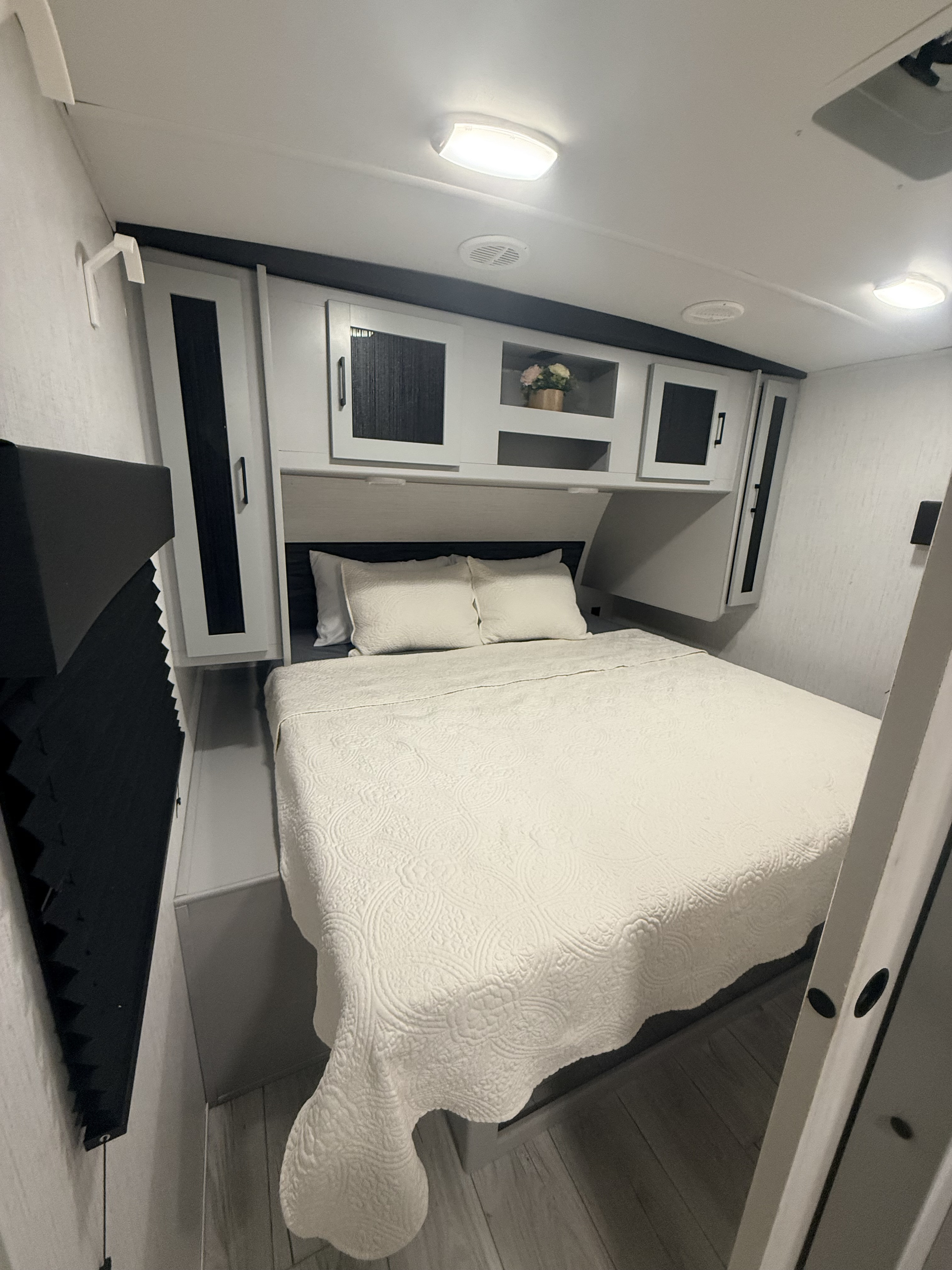 Cozy RV rental bedroom with white quilted bedding, overhead storage, ceiling lights, and a window blind.. Heartland RVs North Trail 2023