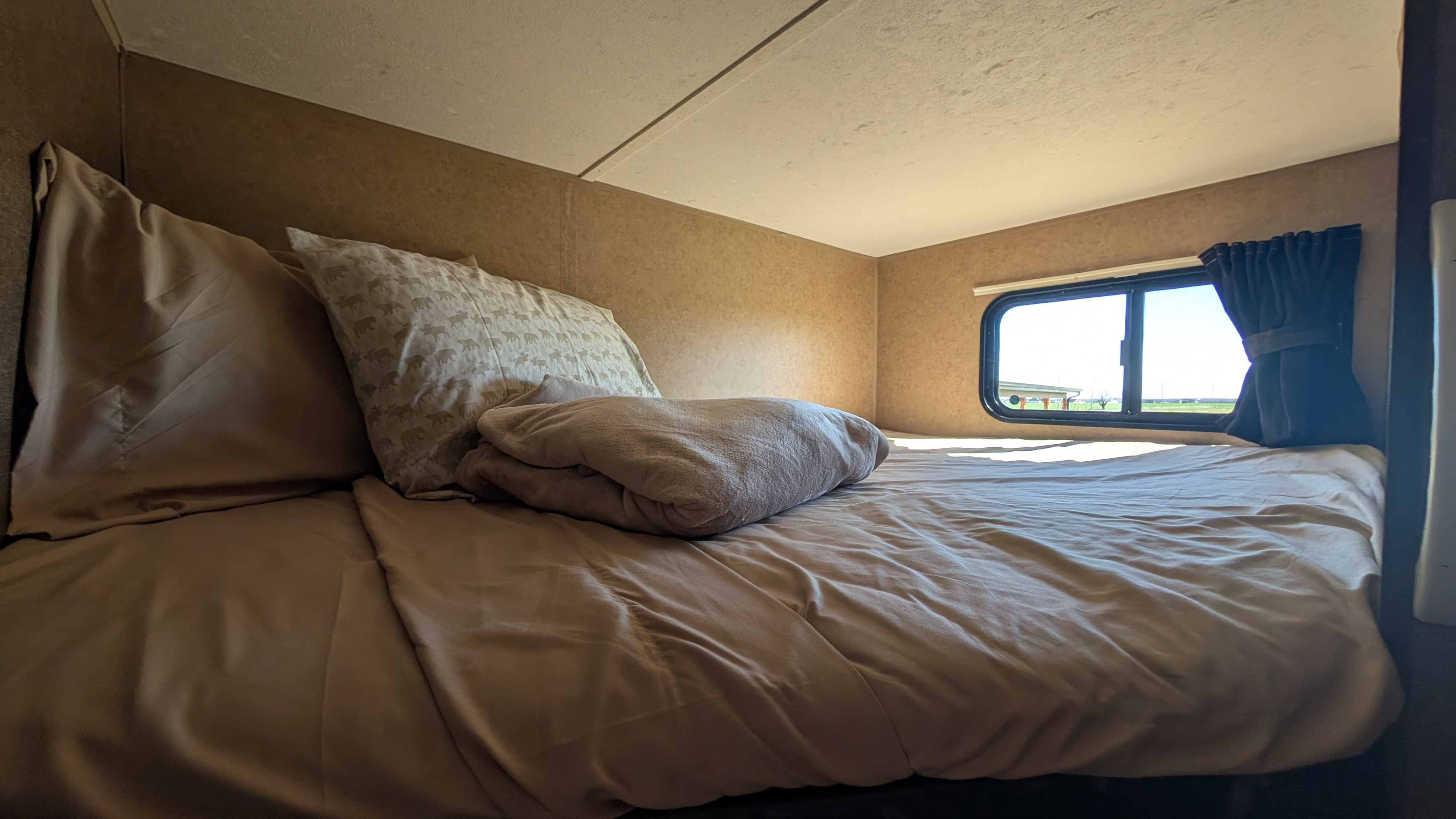 Inviting RV rental bedroom interior with a made bed, patterned pillows, folded blanket, and a sunlit window view.. Starcraft Autumn Ridge 2013