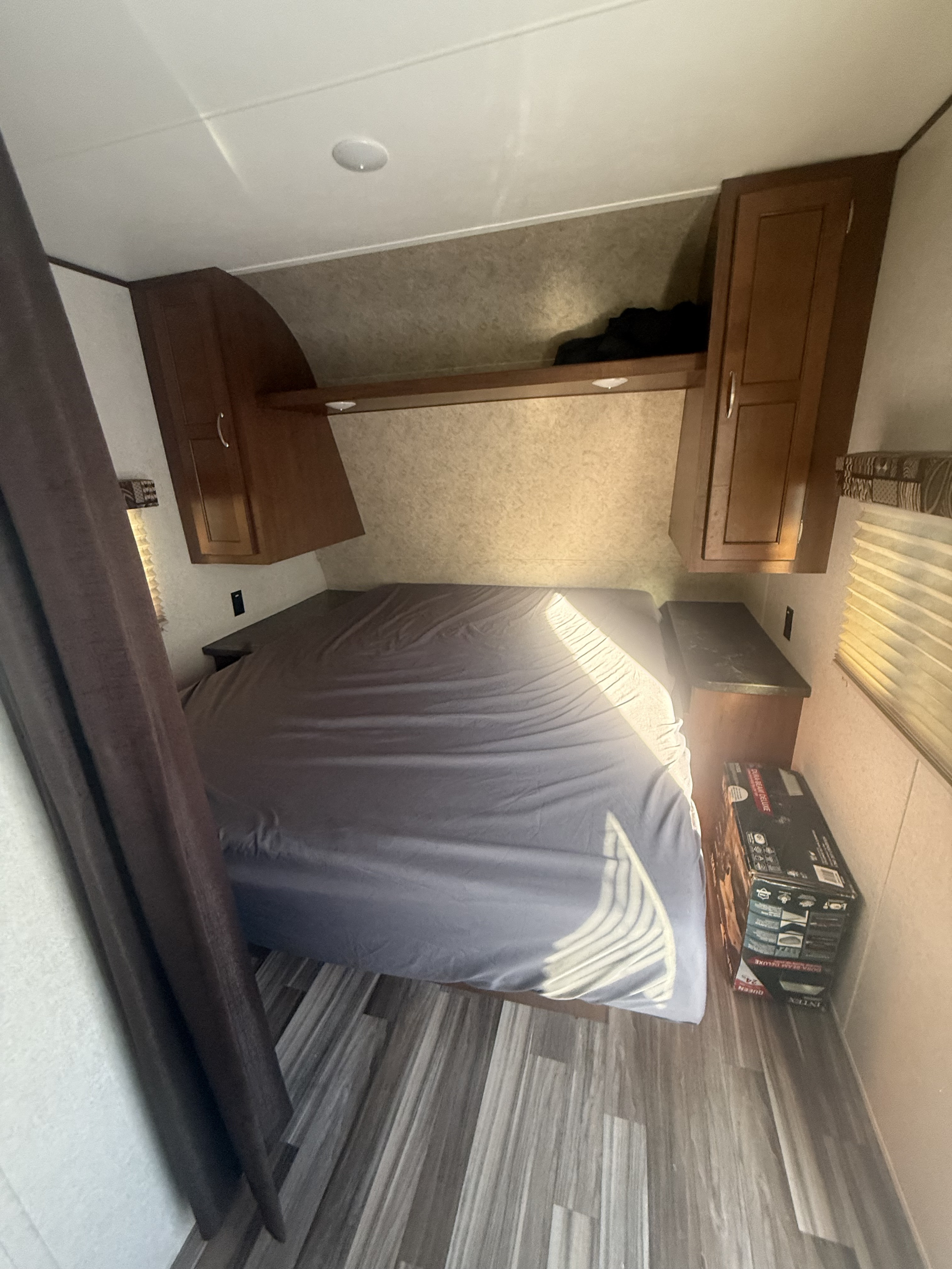 RV rental bedroom: A compact sleeping area with a grey-sheeted bed, overhead cabinets, a small side table, and a window.. Jayco Jay Flight 2017