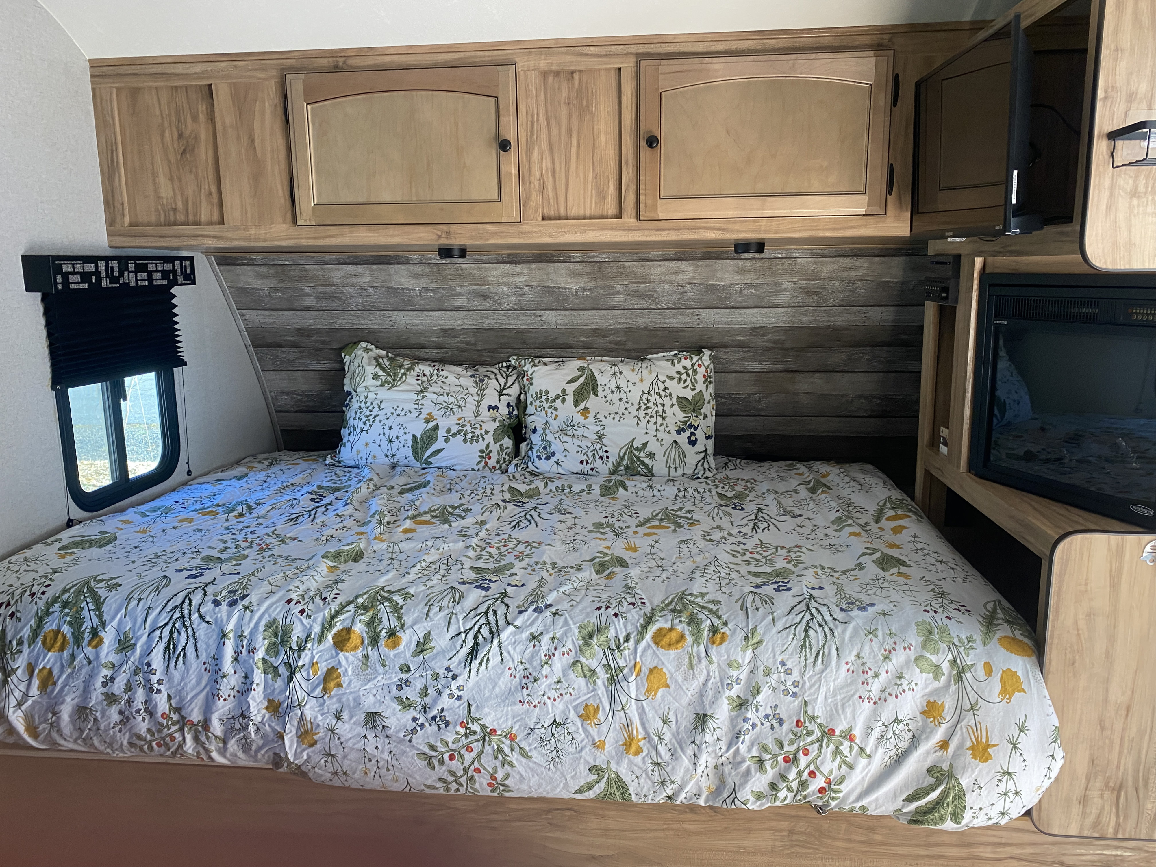 Enjoy a comfortable rv rental experience! This RV bedroom features floral bedding, wood cabinets, a window, and TV.. Forest River Coachmen Freedom Express Pilot 2019