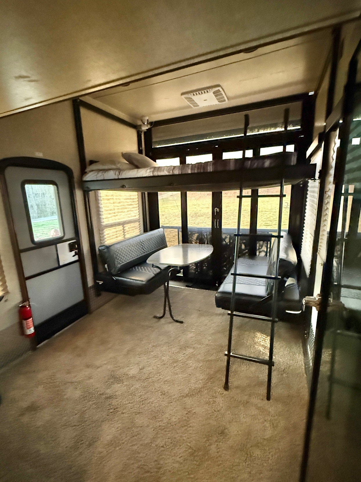 RV rental interior: bunk bed with ladder, dining booth with black benches & table, and an exit door. Carpeted floor.. Keystone Fuzion 2016