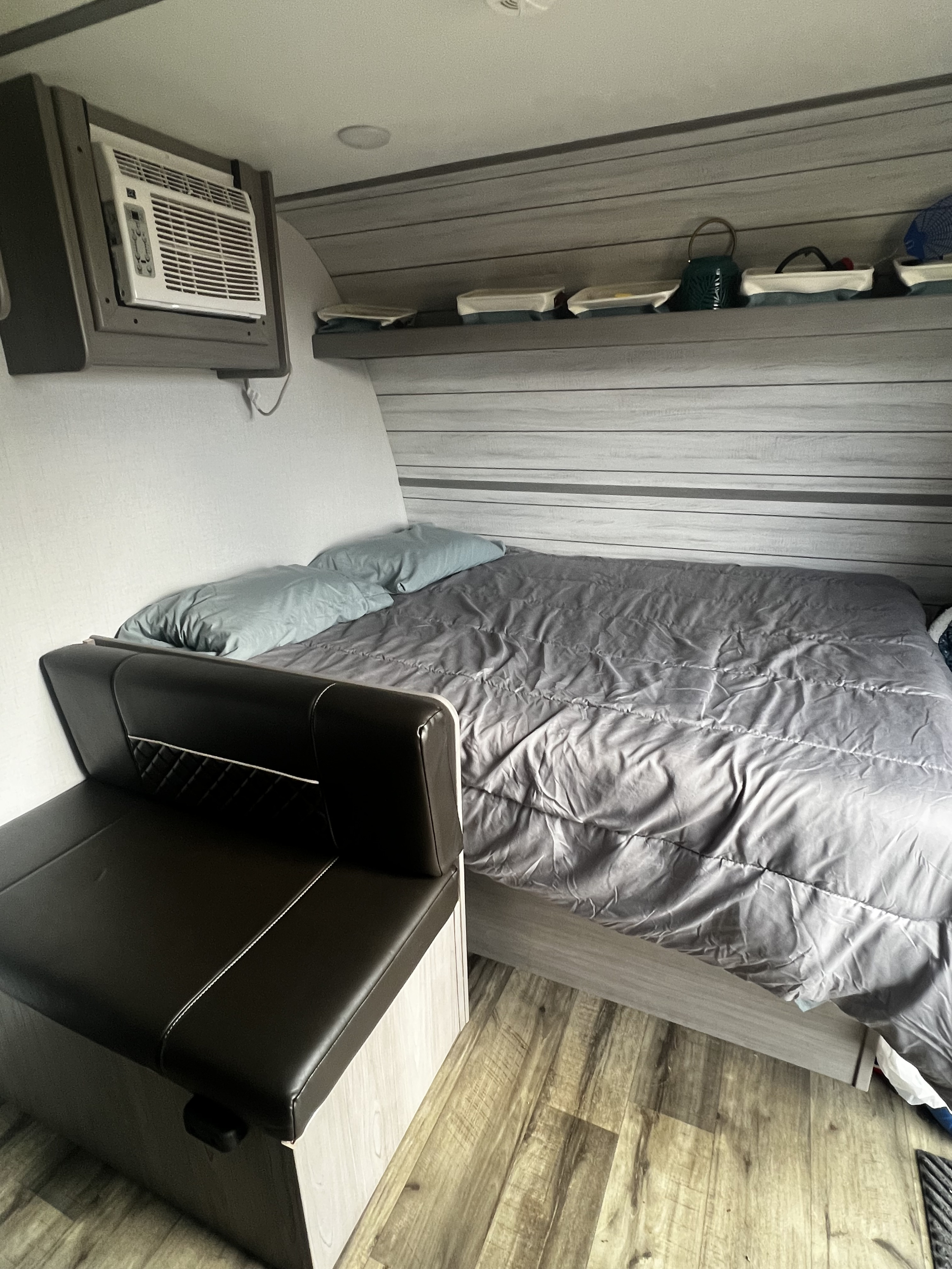 Compact RV rental interior featuring a bed, built-in seating, AC unit, and overhead storage shelf.. Keystone RV Coleman Lantern 17B 2024