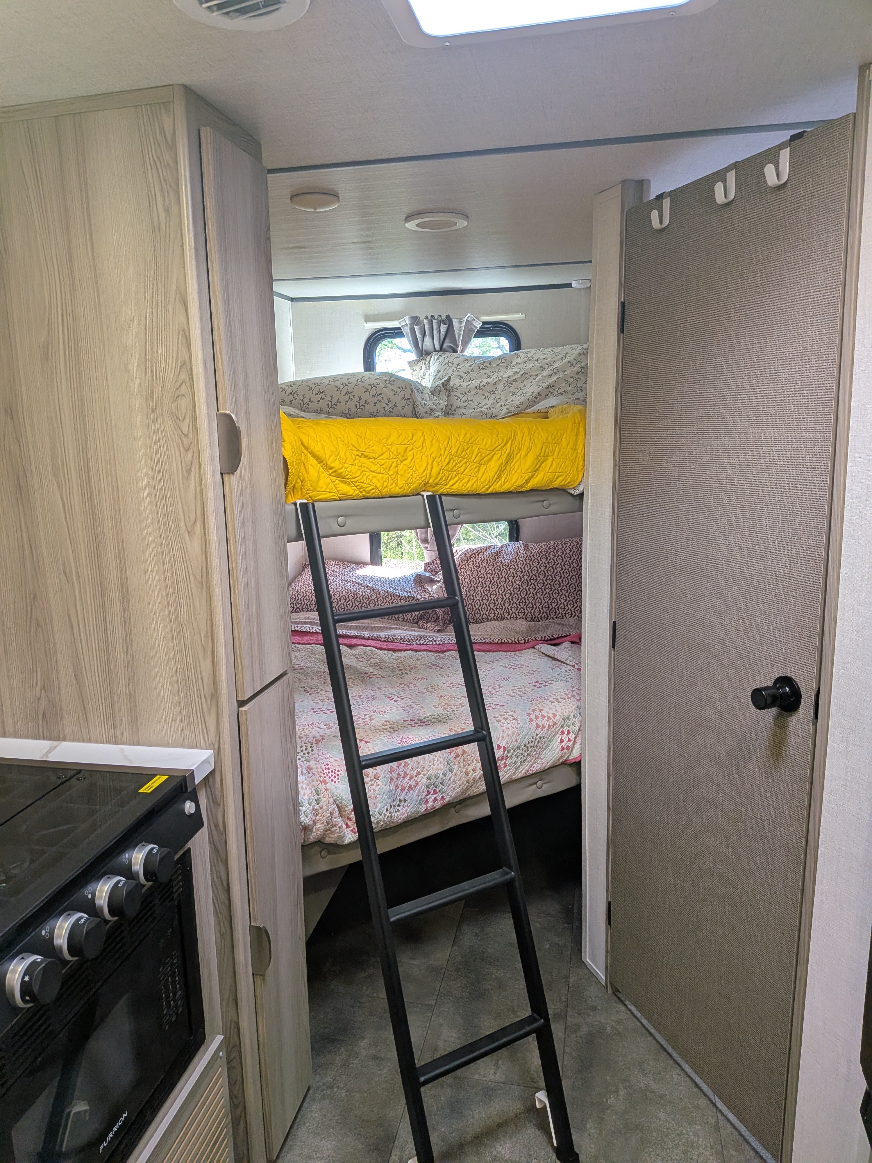 An RV rental interior highlights bunk beds with a ladder, a window, and part of a kitchen stove on the left.. Forest River Salem FSX 266BHLE 2025