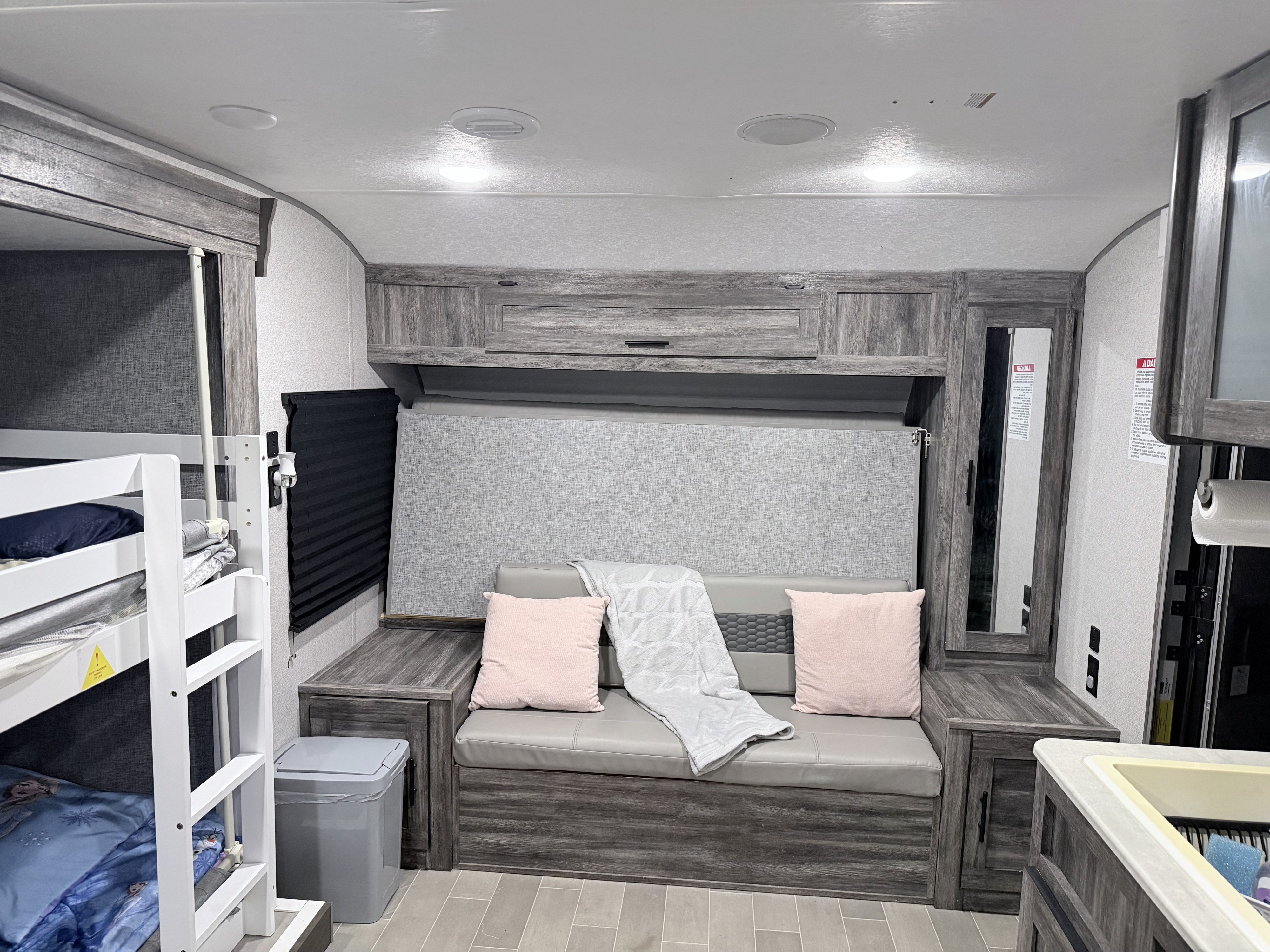 This rv rental interior features bunk beds, a gray sofa with pink pillows, and ample storage, providing a cozy camper living area.. Forest River Wildwood 2021