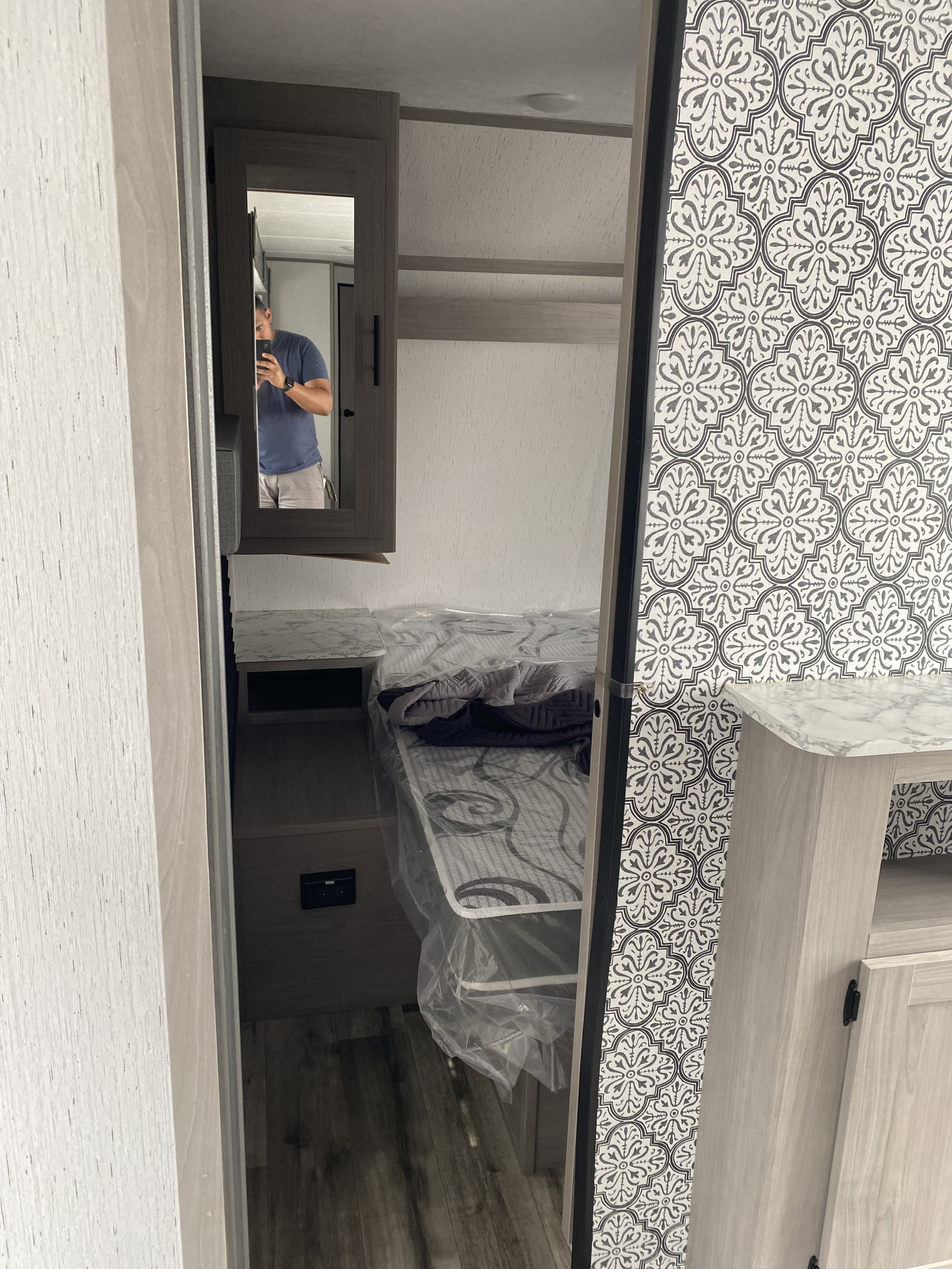 Peeking into a clean RV rental bedroom, featuring a protected bed, smart storage with a mirror, and stylish patterned walls.. Dutchmen Coleman Lantern LT 2023