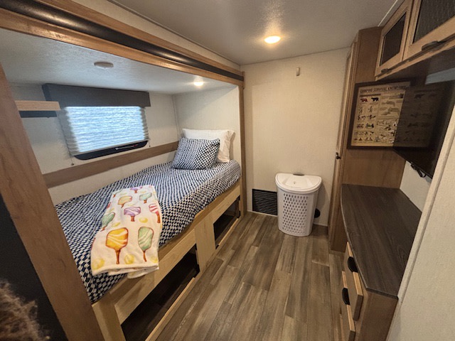 Cozy RV rental bunkhouse: A single bed with patterned bedding, window, under-bed storage, dresser, and laundry hamper.. Forest River Sabre 2024